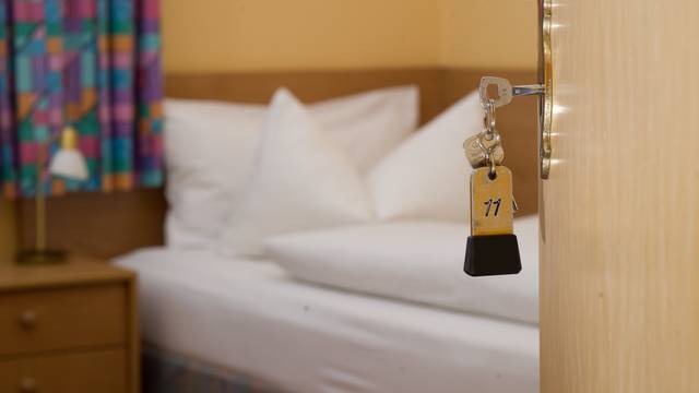 Ein Zimmerschlüssel hängt in einem Gästehaus vor einem Bett im Türschloss.