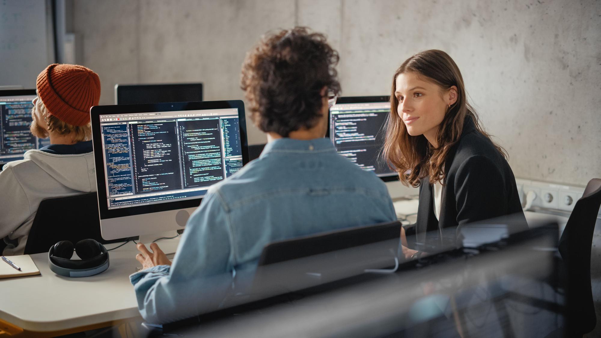 Kolleginnen und Kollegen arbeiten gemeinsam an Bildschirmen mit Programmcode.