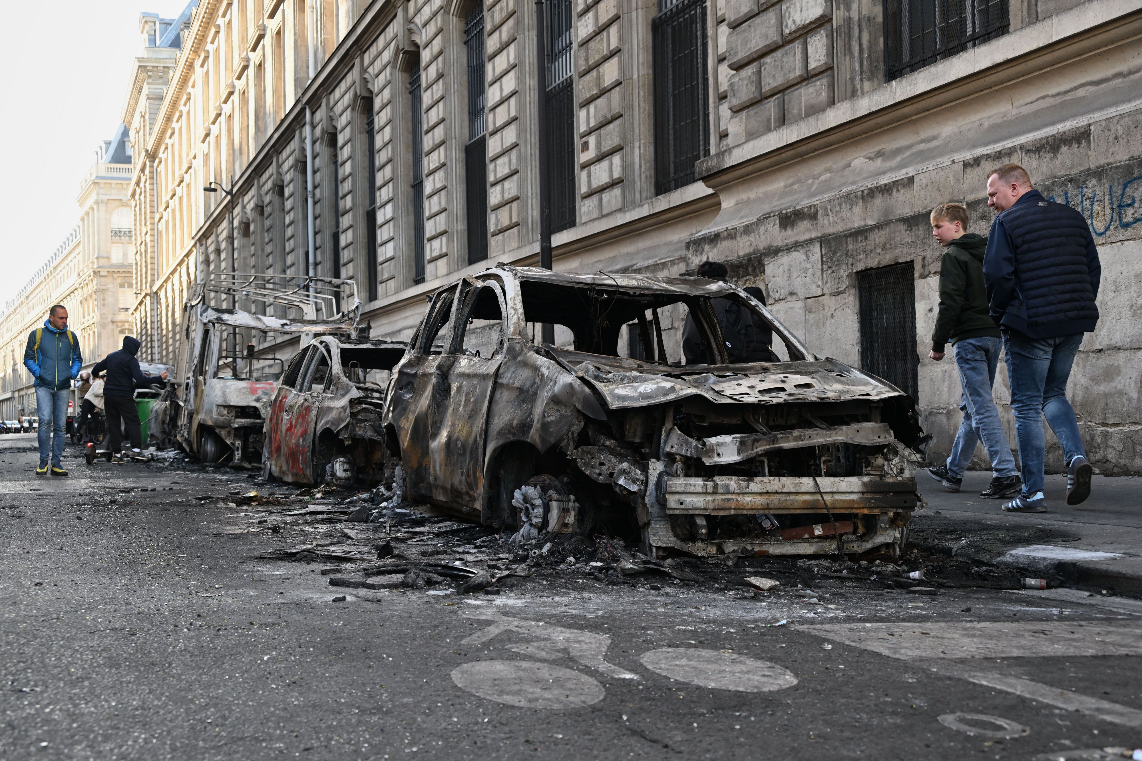 Menschen betrachten am Tag nach einer Demonstration gegen steigende Lebenshaltungskosten verkohlte Autos.