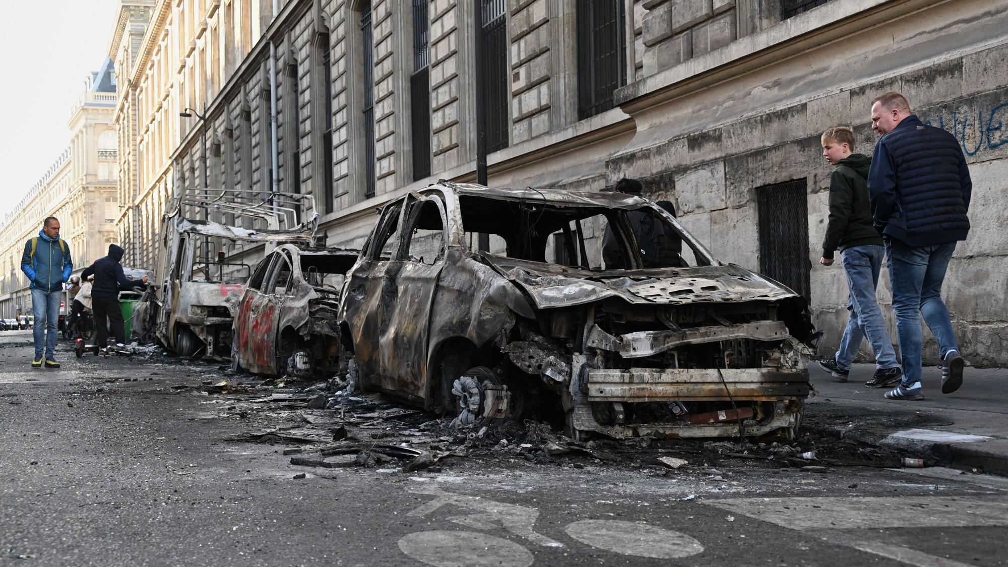 Menschen betrachten am Tag nach einer Demonstration gegen steigende Lebenshaltungskosten verkohlte Autos.