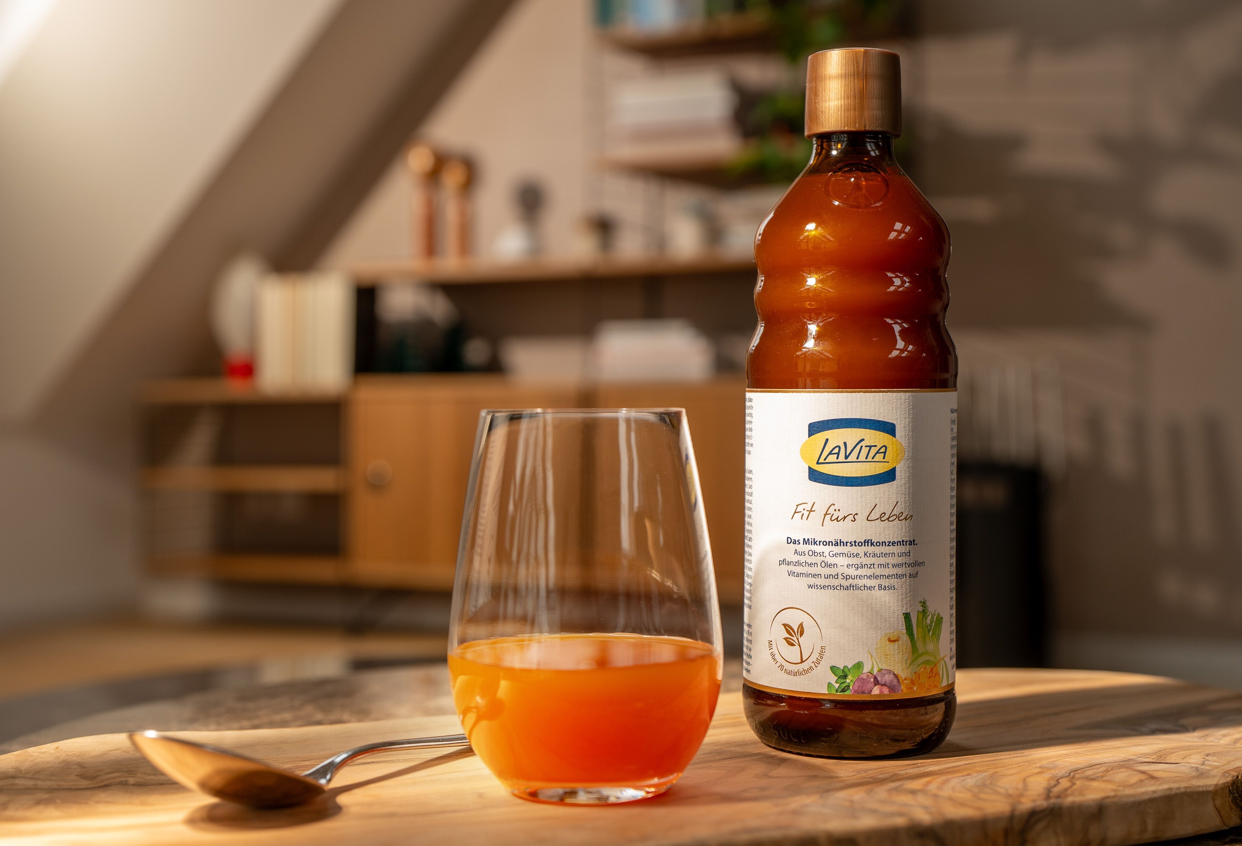 Flasche LaVita Mikronährstoffkonzentrat mit einem Glas der verdünnten Zubereitung und einem Löffel auf einem Holzbrett