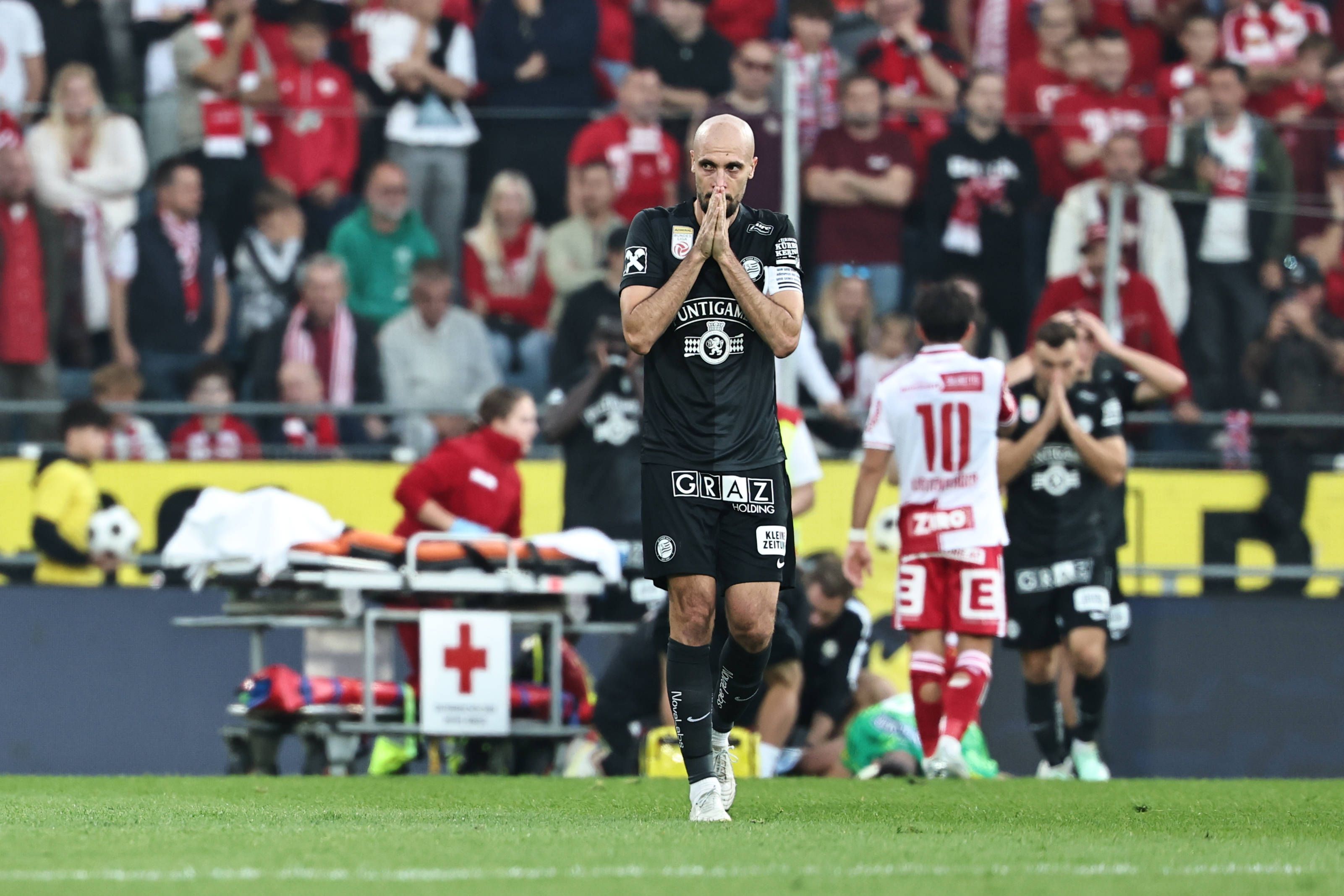 Ein Spieler von Sturm Graz zeigt sich schockiert von der Verletzung seines Teamkollegen Daniil Khudyakov, der im Hintergrund behandelt wird.