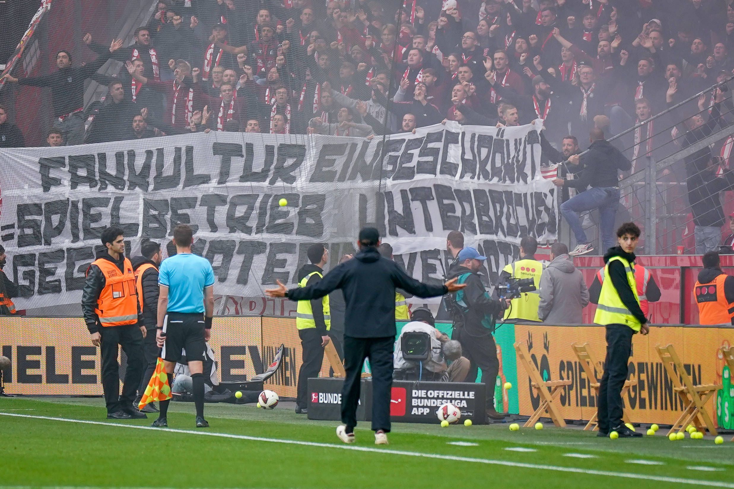 Spielunterbrechung in Leverkusen: SC-Freiburg-Trainer Julian Schuster steht mit ausgebreiteten Armen vor dem Gästeblock, nachdem Fans Tennisbälle auf das Spielfeld geworfen haben.