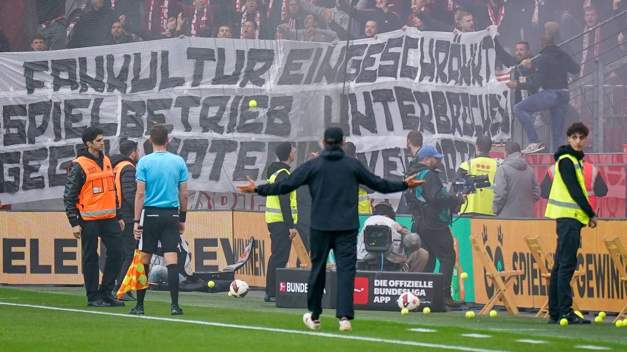Spielunterbrechung in Leverkusen: SC-Freiburg-Trainer Julian Schuster steht mit ausgebreiteten Armen vor dem Gästeblock, nachdem Fans Tennisbälle auf das Spielfeld geworfen haben.
