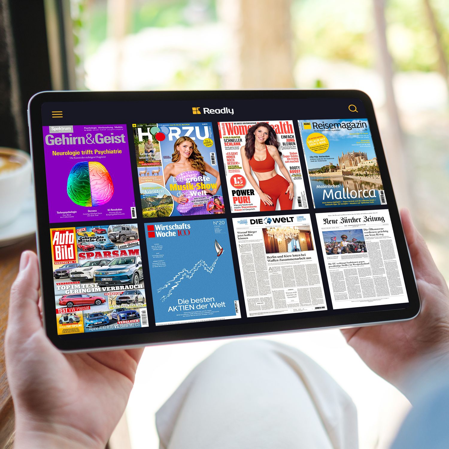 Zeitschriften und Magazine auf einem Tabletdisplay in der Readly App, gehalten von zwei Händen.