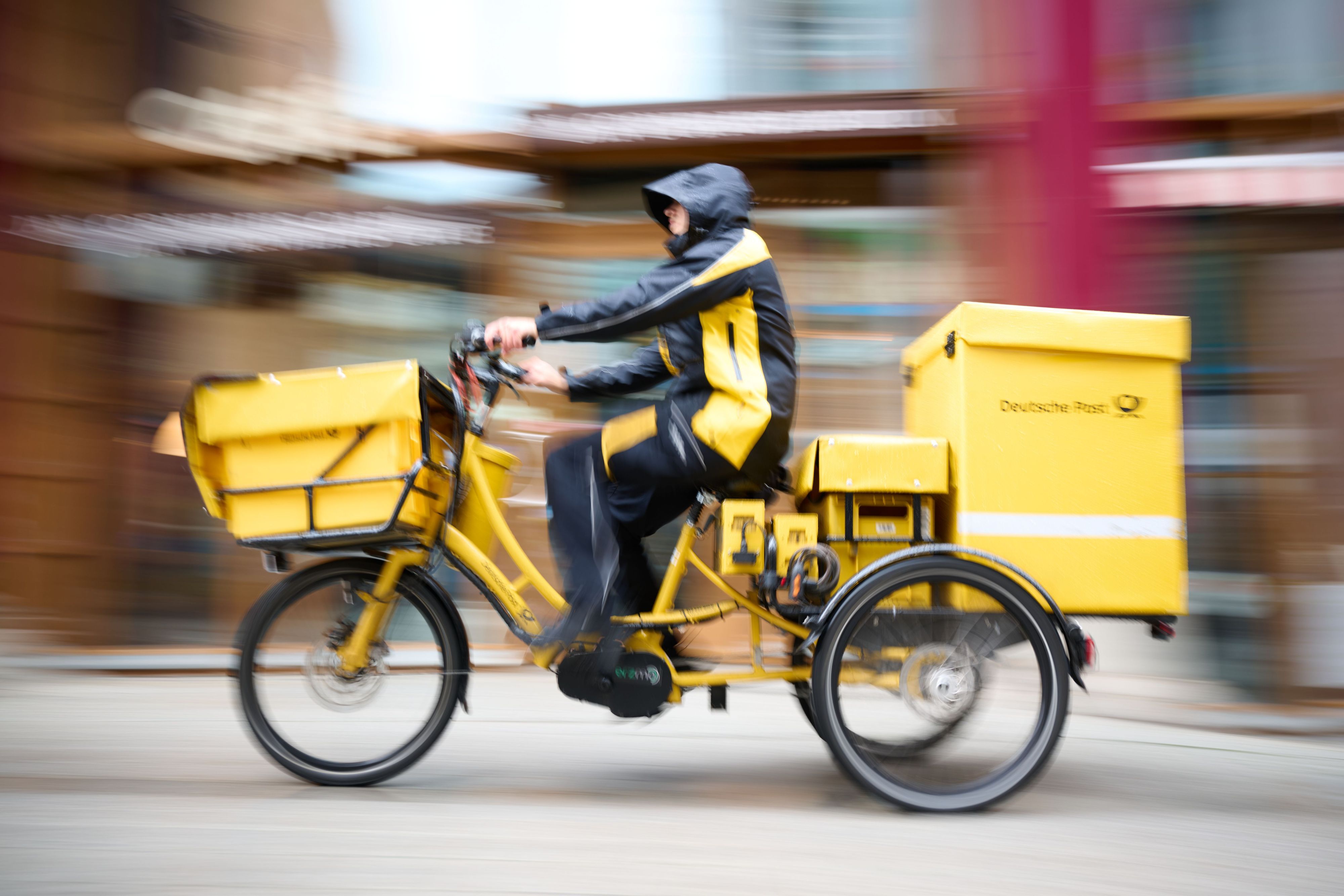 Ein Postbote stellt Briefe mit einem Postfahrrad zu.