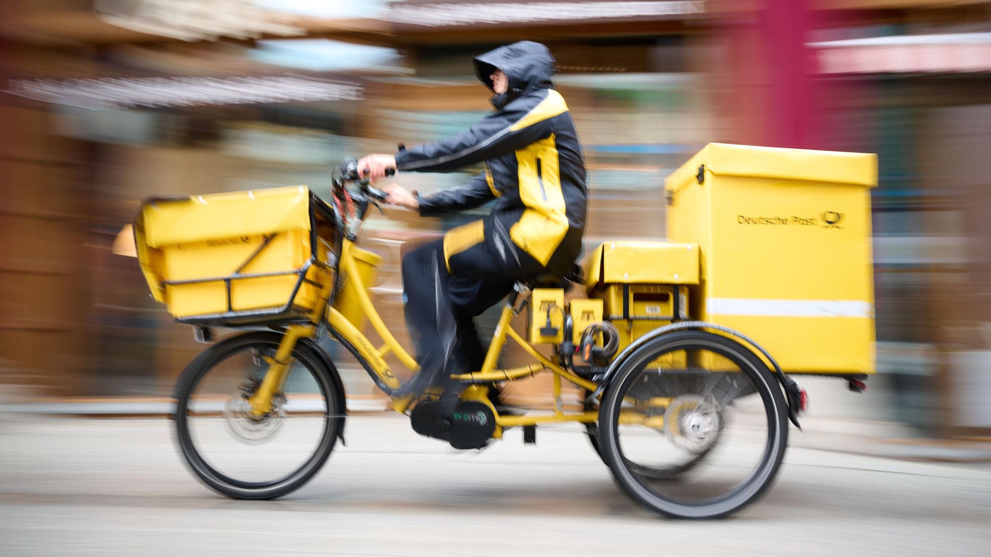 Ein Postbote stellt Briefe mit einem Postfahrrad zu.