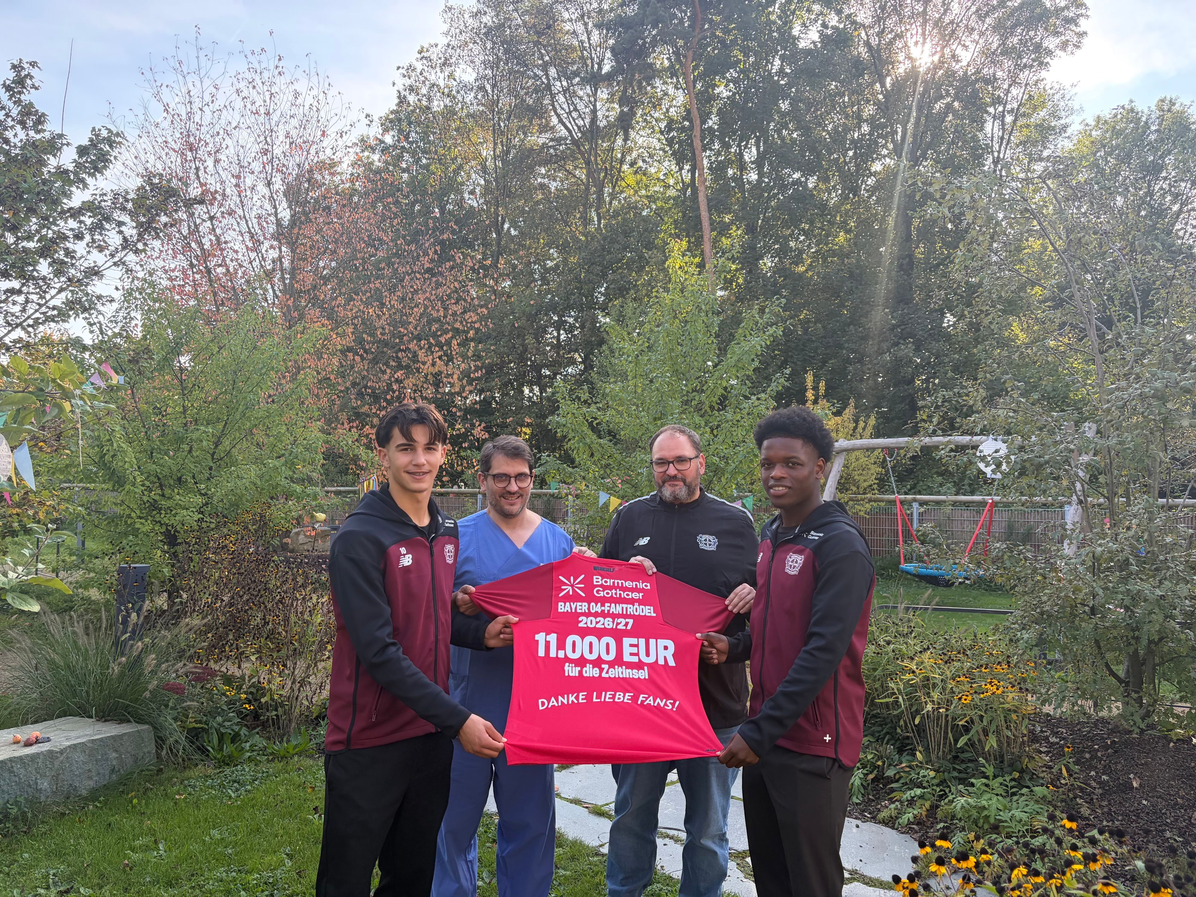 Gabriel Minutillo (l.) und Ivan Massek (r.) von der U19-Mannschaft übergeben mit Frank Linde (2. v.r.) vom Sozial-Team von Bayer 04 das Spenden-Trikot an Dr. Dejan Vlajnic (2. v.l.).