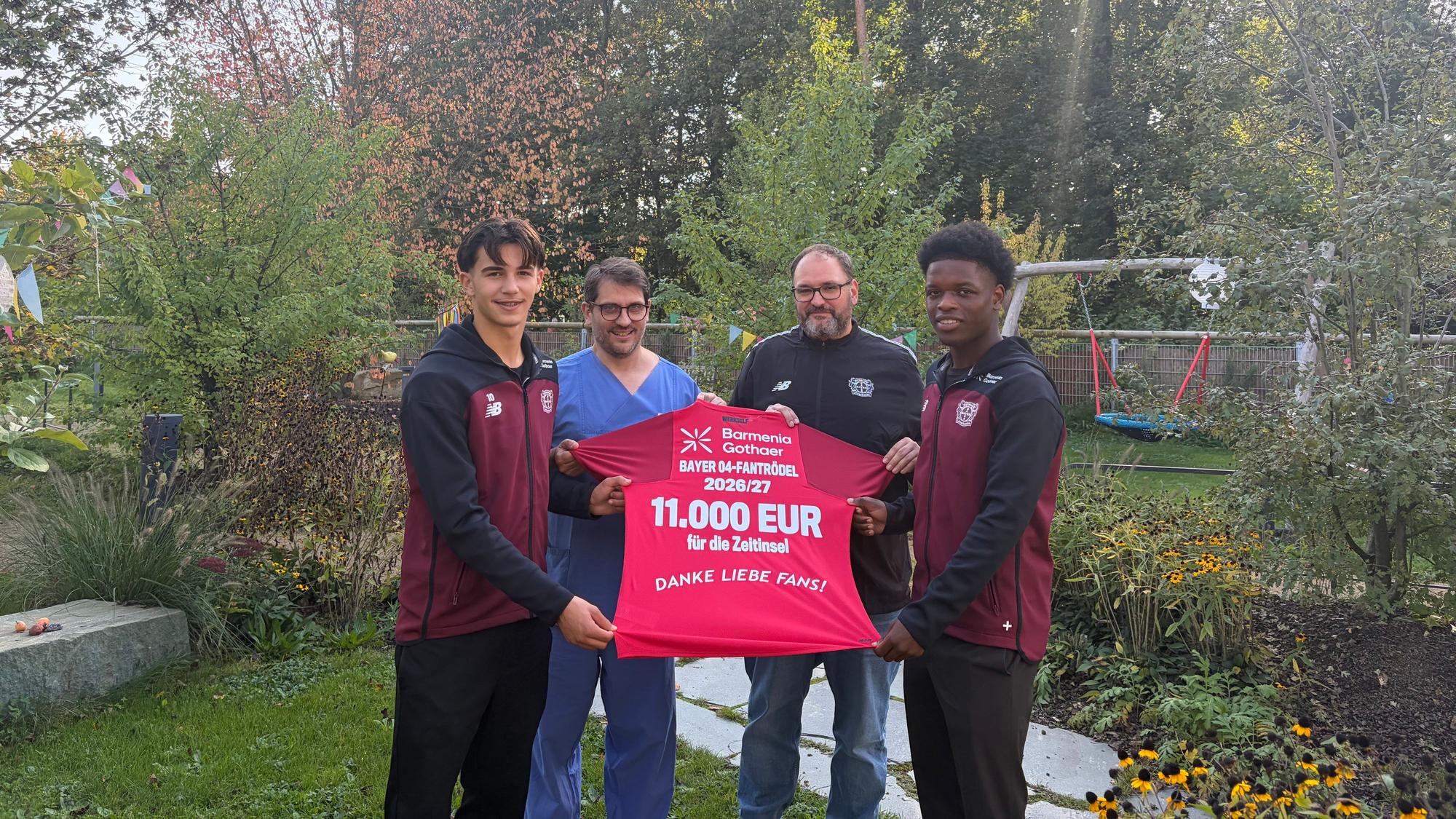 Gabriel Minutillo (l.) und Ivan Massek (r.) von der U19-Mannschaft übergeben mit Frank Linde (2. v.r.) vom Sozial-Team von Bayer 04 das Spenden-Trikot an Dr. Dejan Vlajnic (2. v.l.).