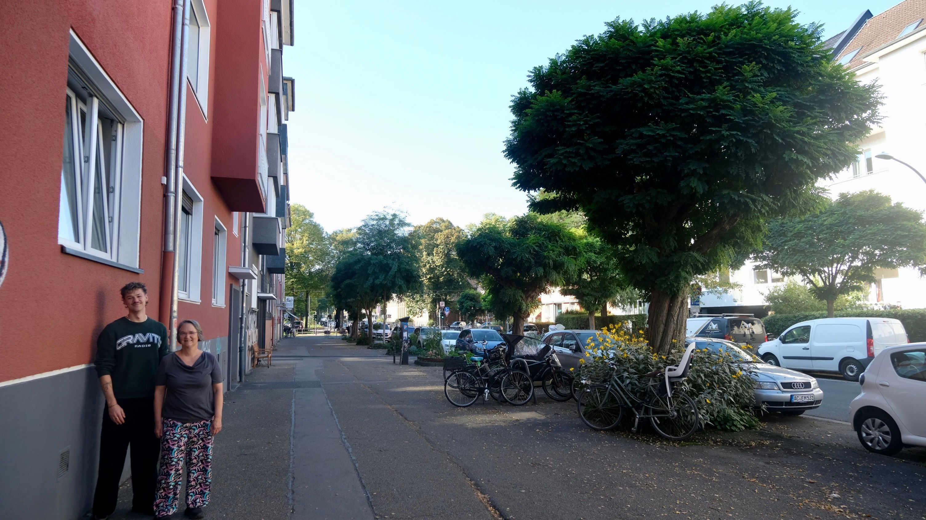 Ein Mann und eine Frau stehen vor einem Fallrohr an einer Hausfassade.