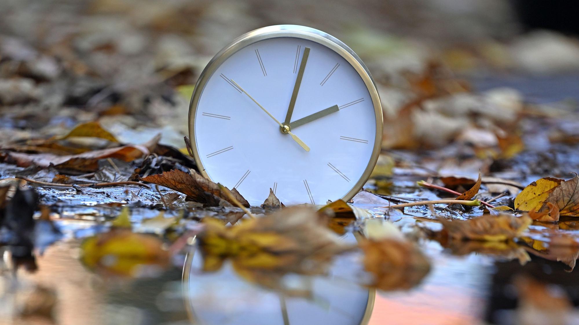Eine Uhr spiegelt sich im blätterbedeckten Wasser. Mit Beginn der Winterzeit werden in Deutschland und den meisten anderen Ländern Europas am Sonntagmorgen (25. Oktober) die Uhren von 3.00 Uhr auf 2.00 Uhr zurückgestellt.
