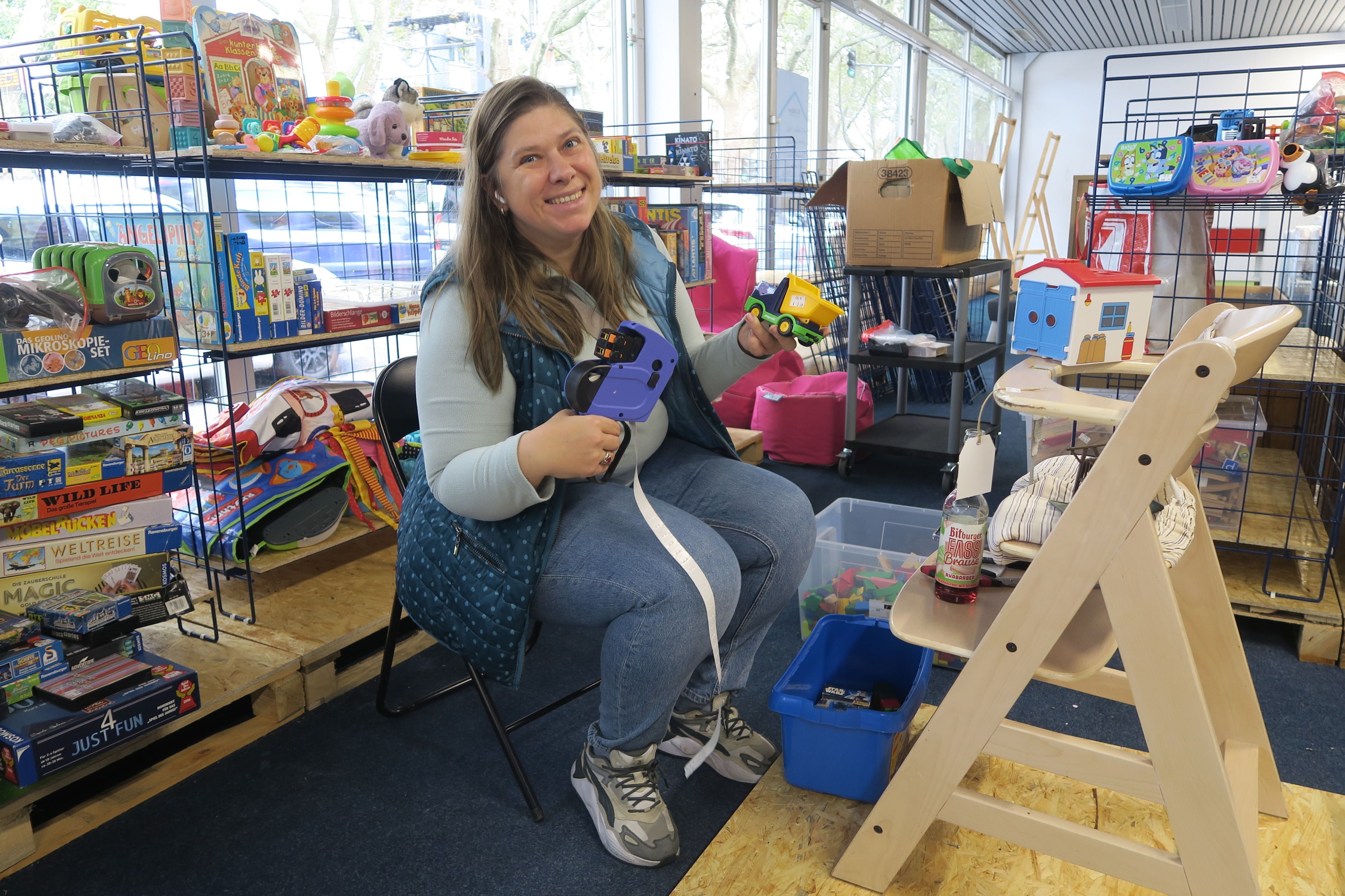 Eine Frau sitzt auf einem Stuhl zwischen Regalen voller Kinderspielzeug.
