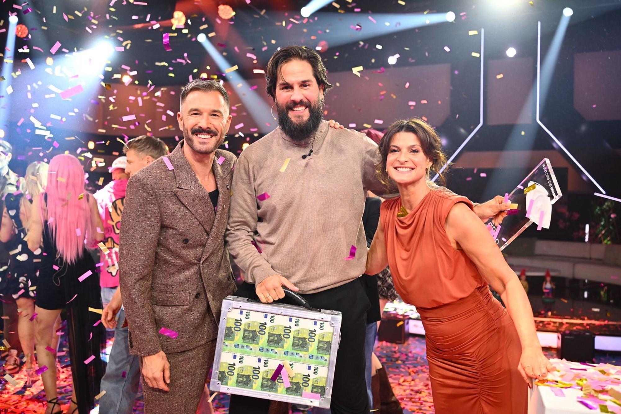 Maurice Dziwak (Mitte) bekommt von Jochen Schropp und Marlene Lufen den Pokal und 100.000 Euro überreicht. (Bild: Joyn/Willi Weber)