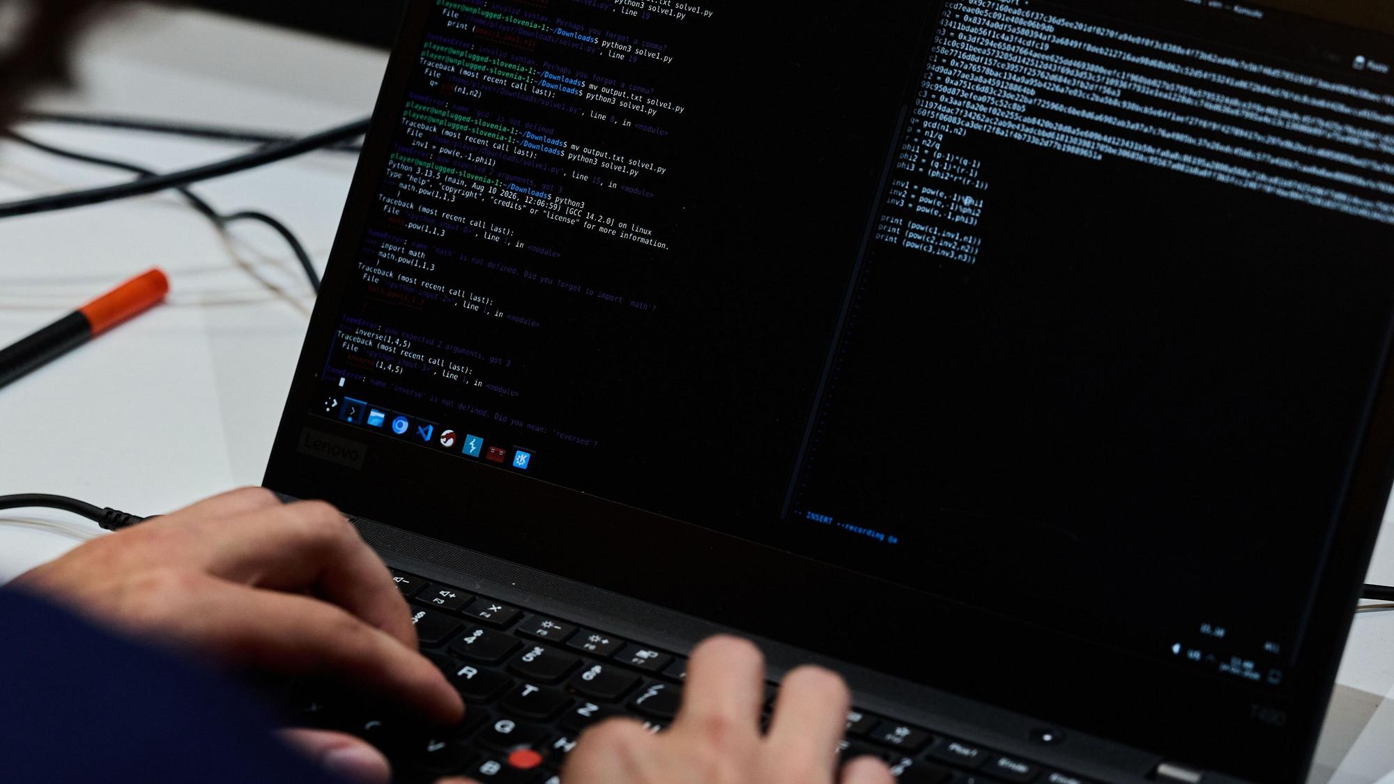 Symbolbild: Hand vor dem Laptop, auf dem Codes zu sehen sind.