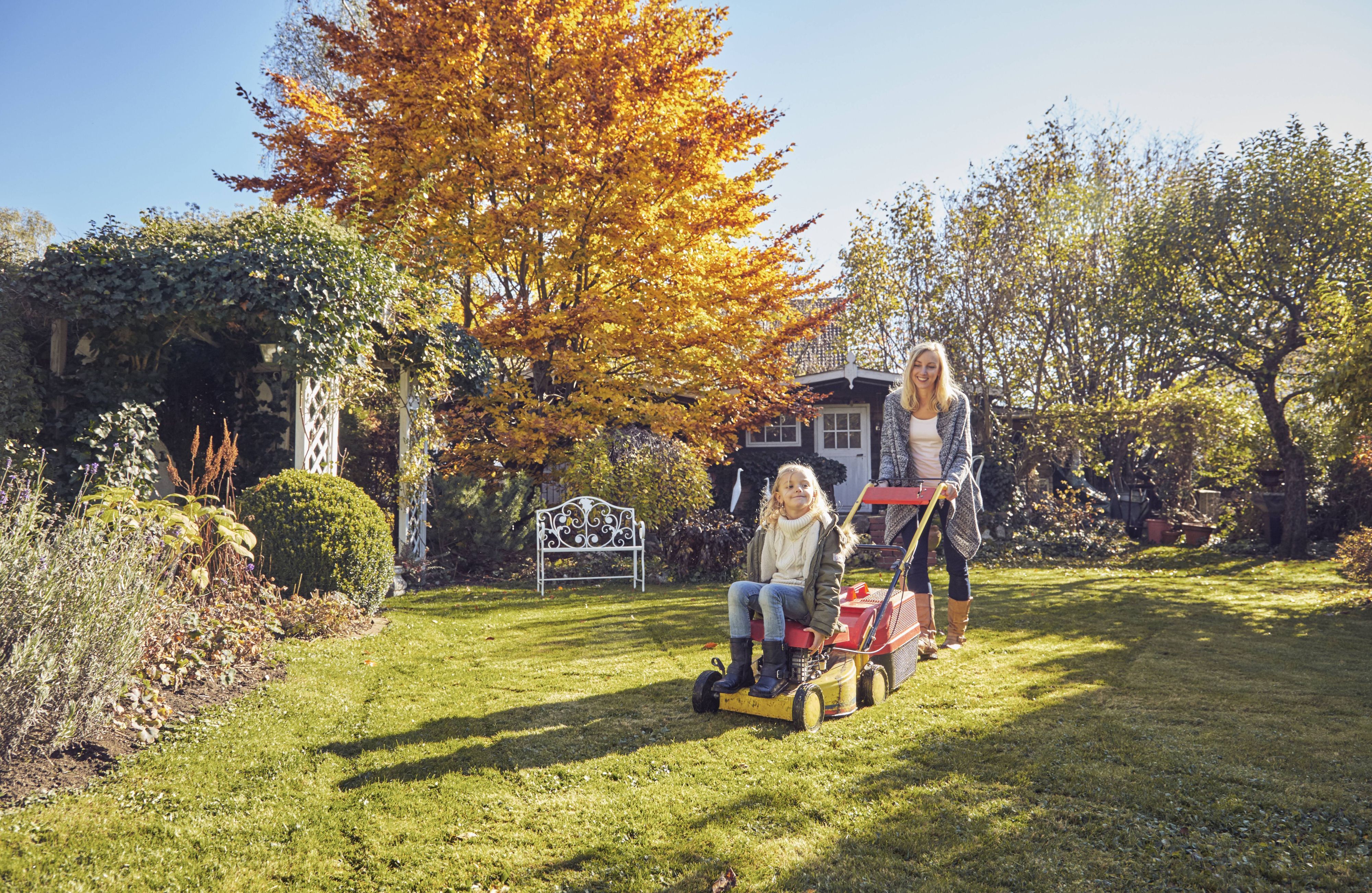 Mutter und Tochter mit einem Rasenmäher im Garten