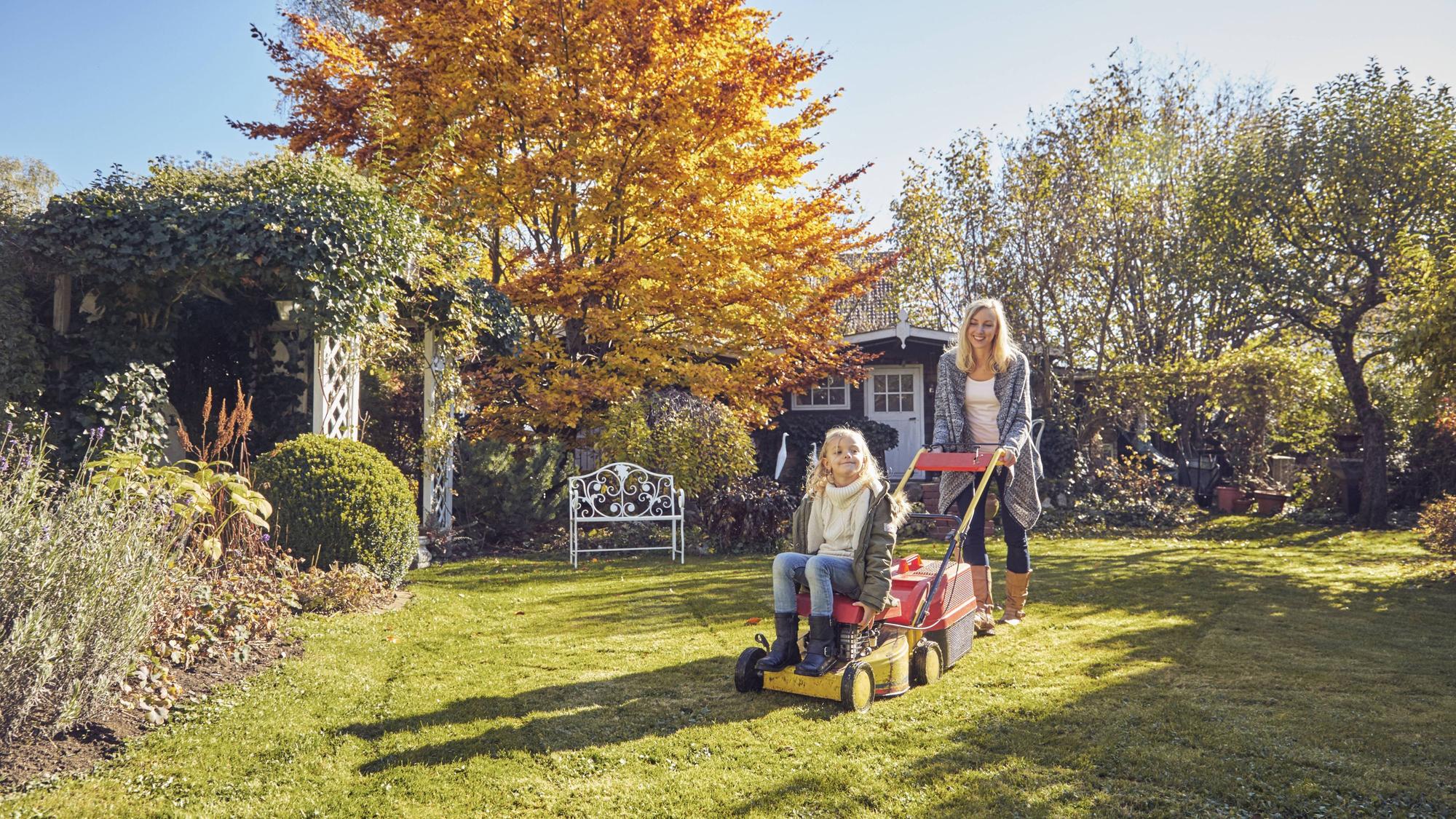 Mutter und Tochter mit einem Rasenmäher im Garten