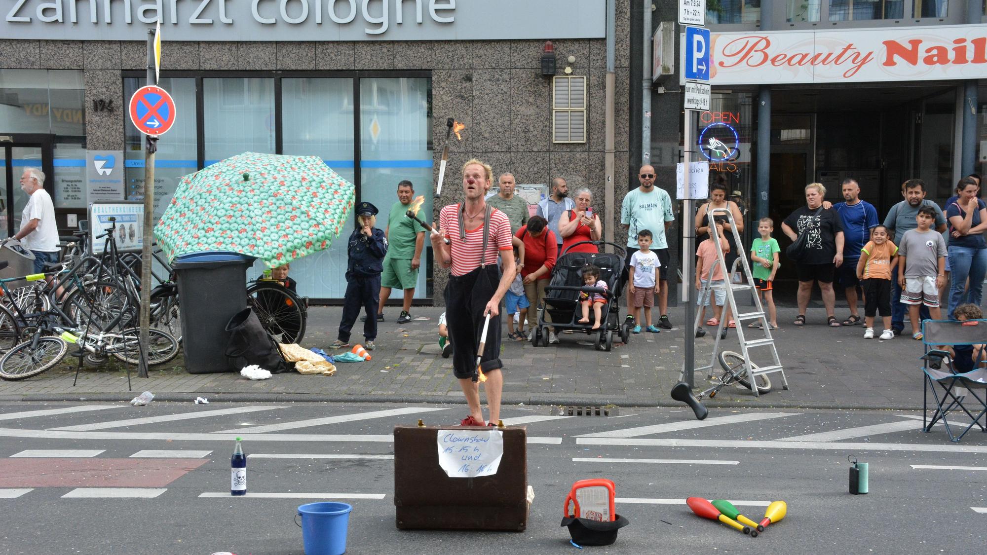 Ein Mann im Clowns-Kostüm jongliert vor Publikum mit Fackeln.