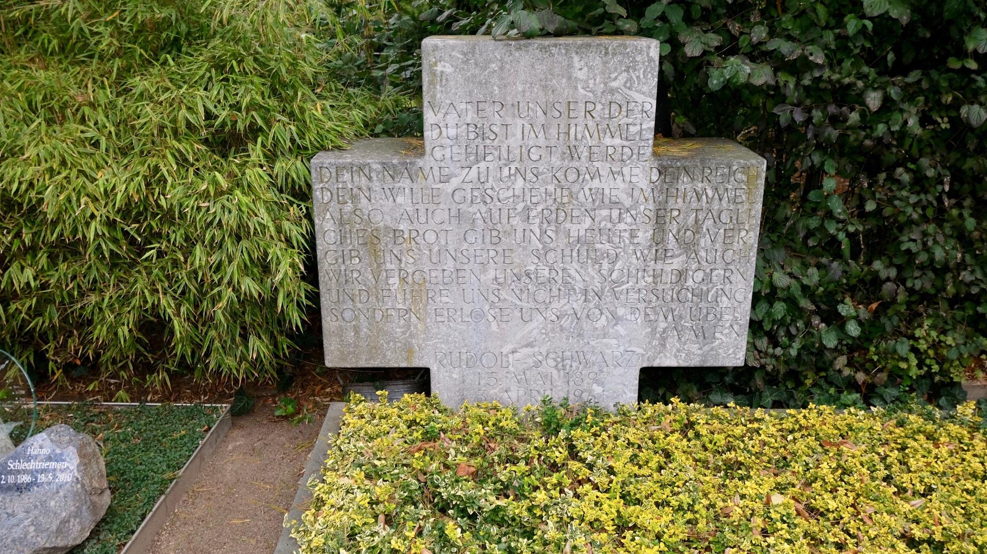 Ein breites Kreuz aus Stein steht auf einer Grabstätte.