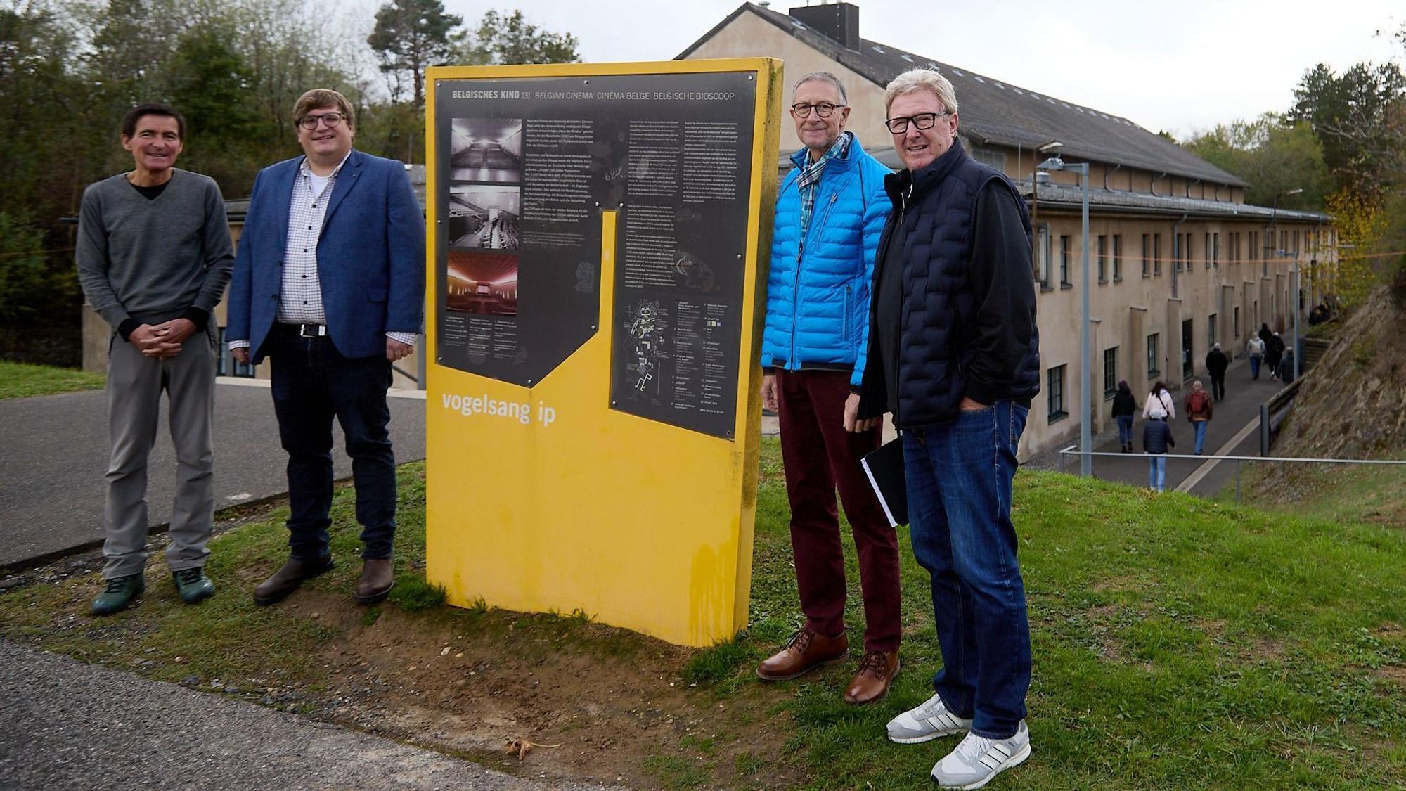 Die genannten Personen stehen vor einer Info-Tafel mit gelbem Sockel auf dem Vogelsang-Gelände.