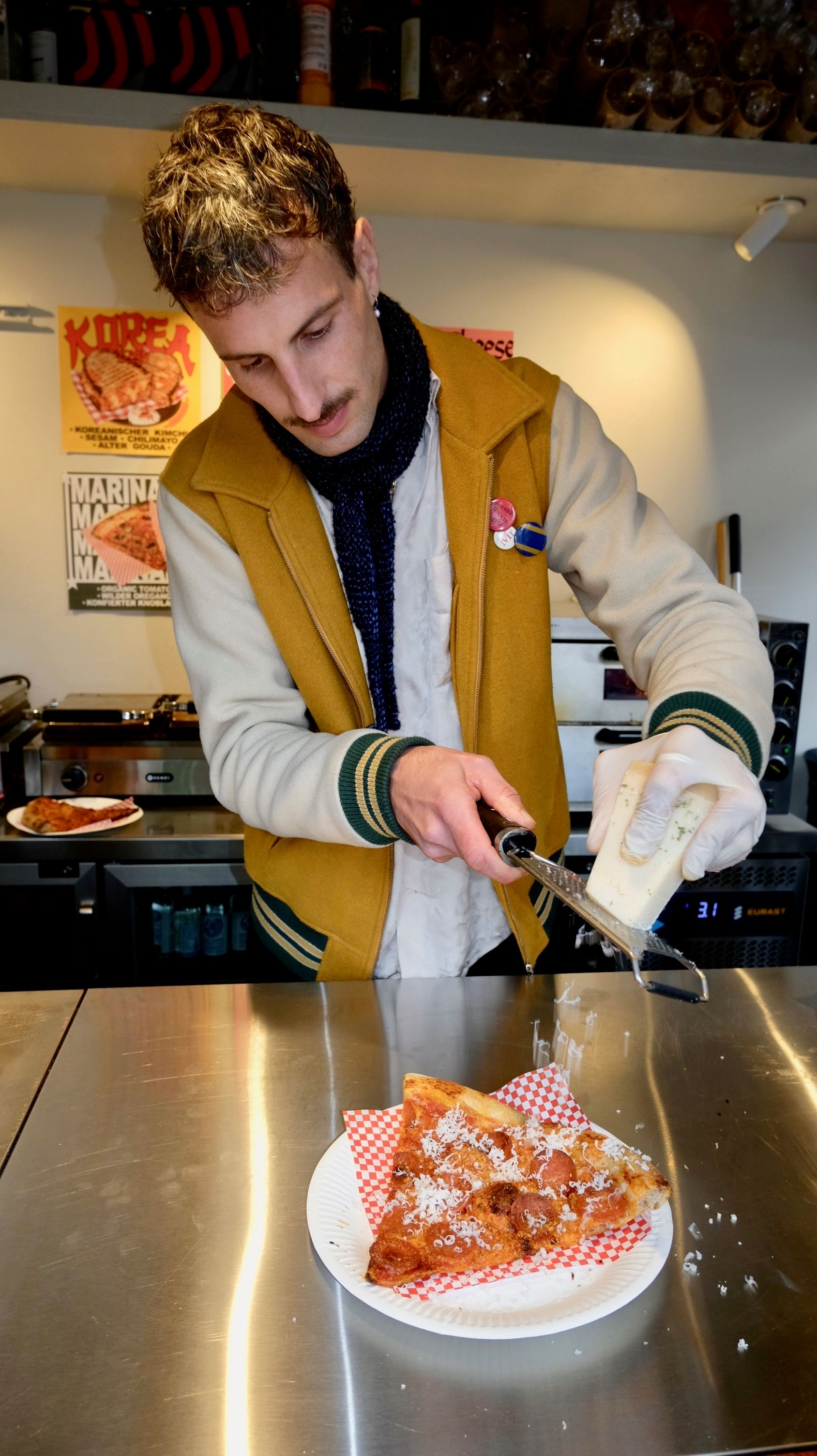 Ein junger Mann reibt Parmesan auf ein Pizza-Stück.