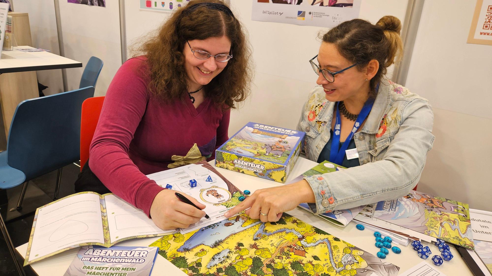 Zwei Frauen sitzen mit einem Spiel an einem Tisch auf der Spielemesse in Essen.
