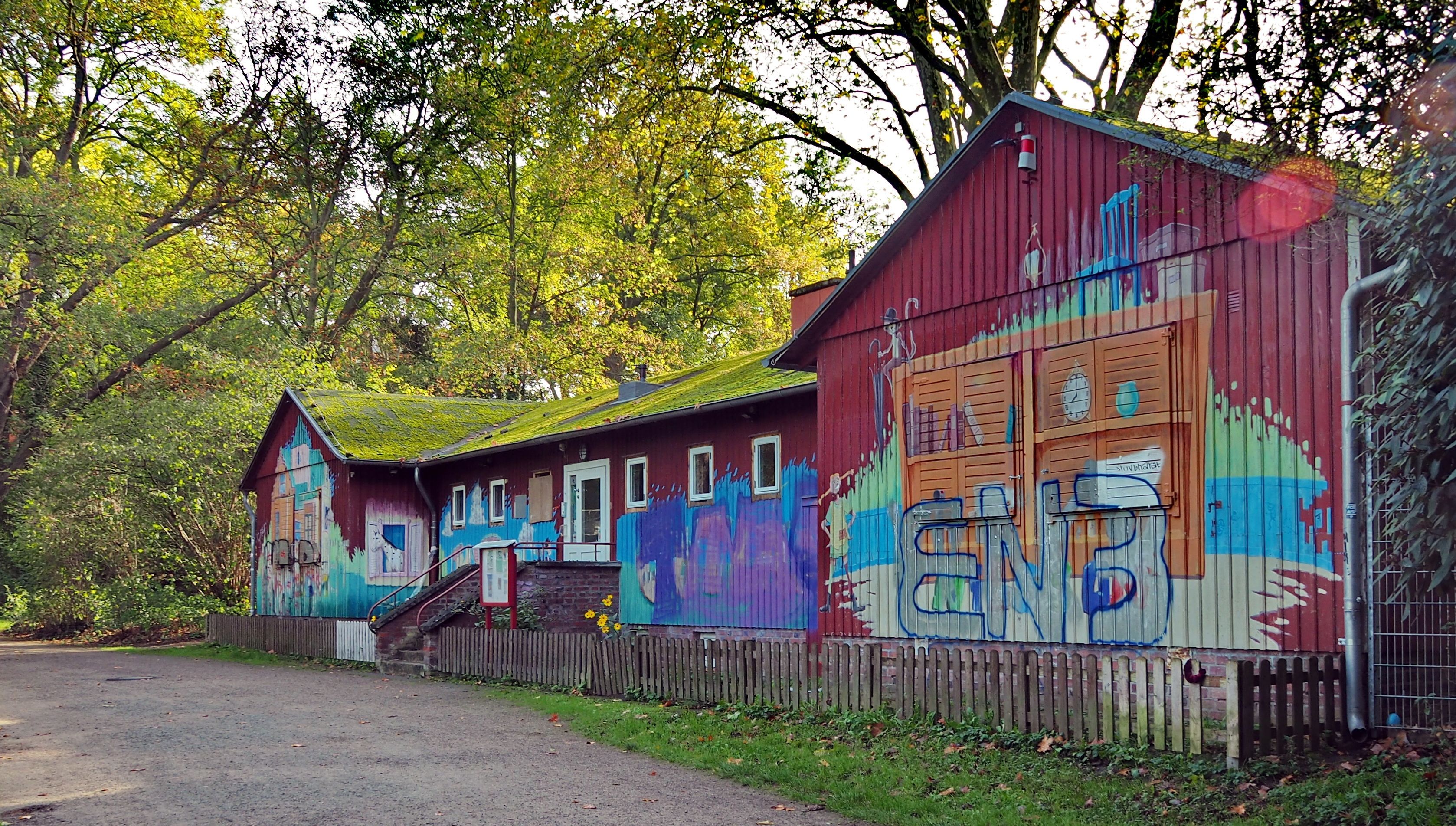 Ein rotes Holzhaus mit bunter Bemalung steht inmitten von Bäumen.