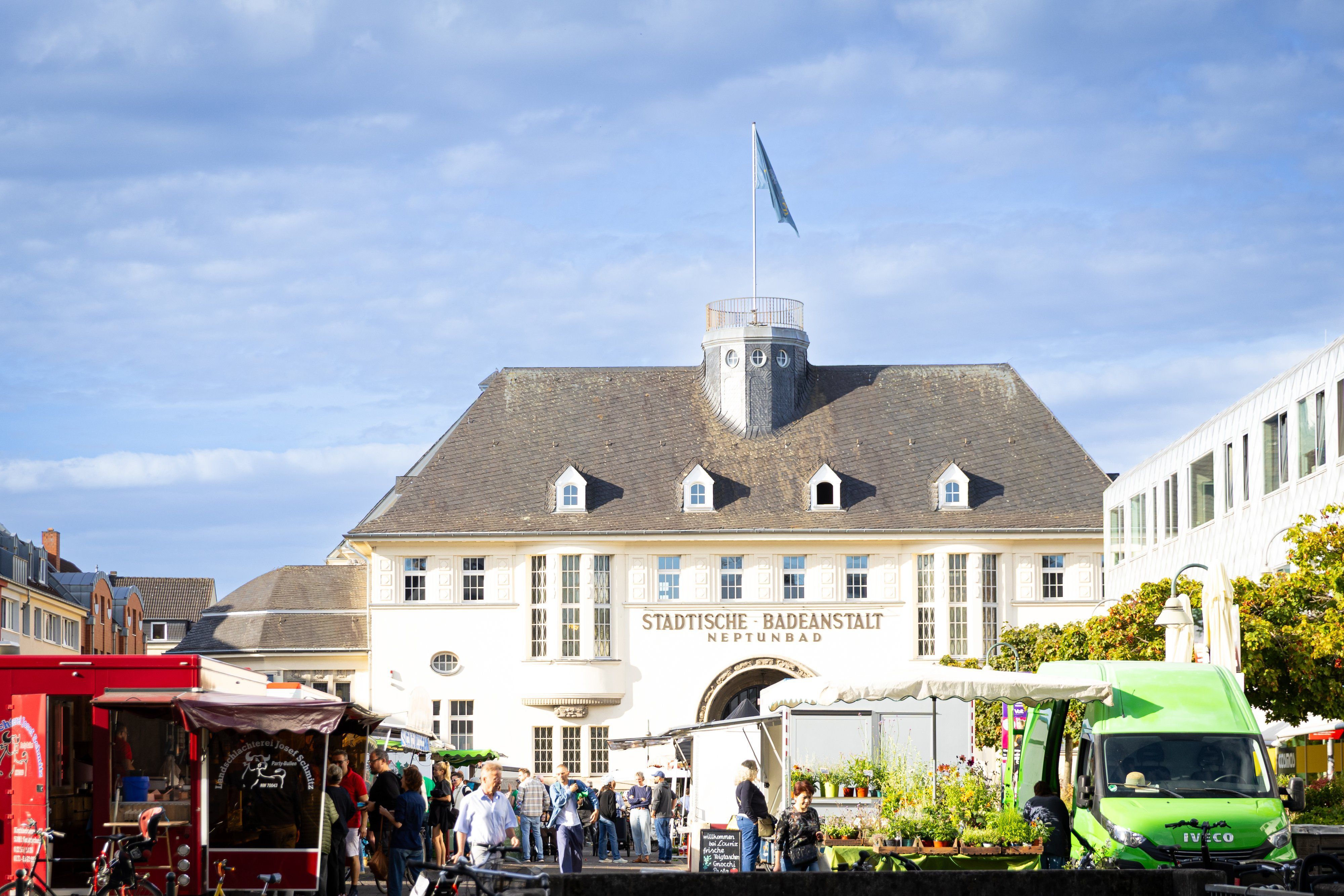 Wochenmarkt mit Ständen und Besuchern vor dem Neptunbad