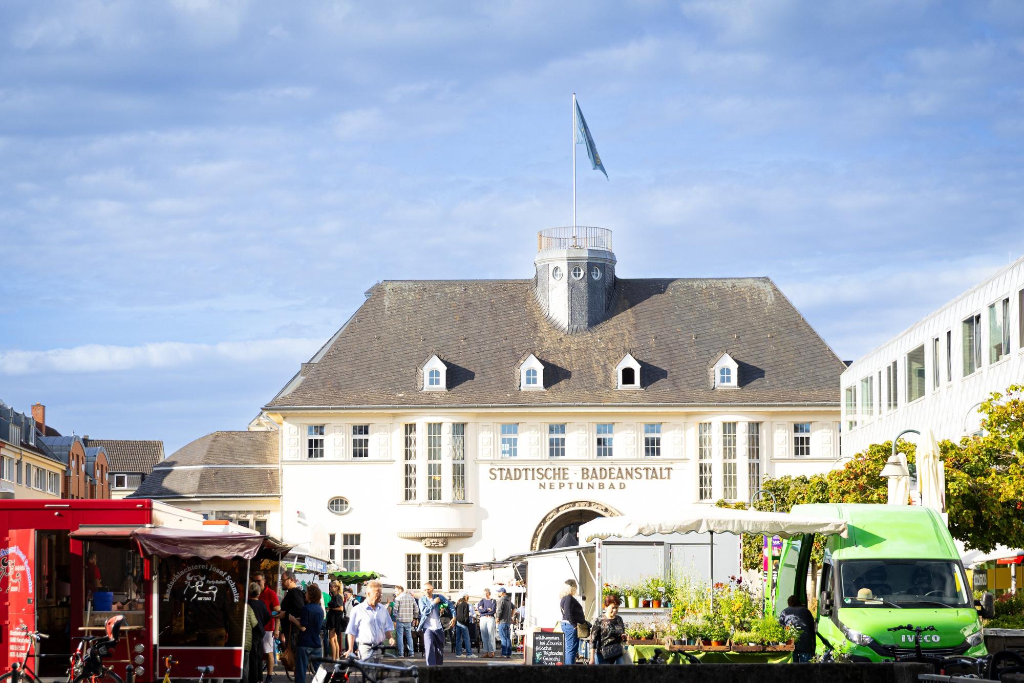Wochenmarkt mit Ständen und Besuchern vor dem Neptunbad