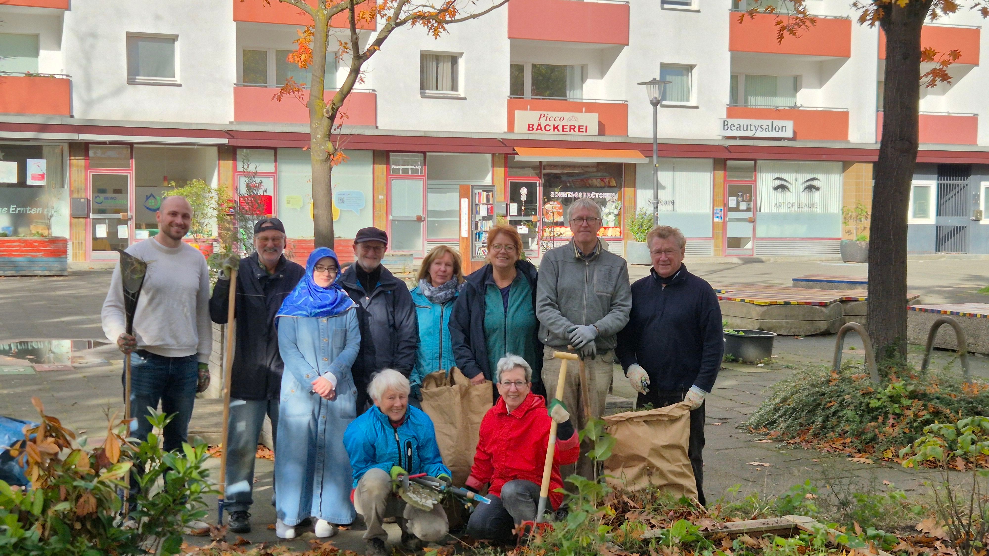 Eine Gruppe von zehn Menschen posiert mit Harken, Laubsäcken und Gartenhandschuhen nach einer gemeinsamen Gartenaktion.