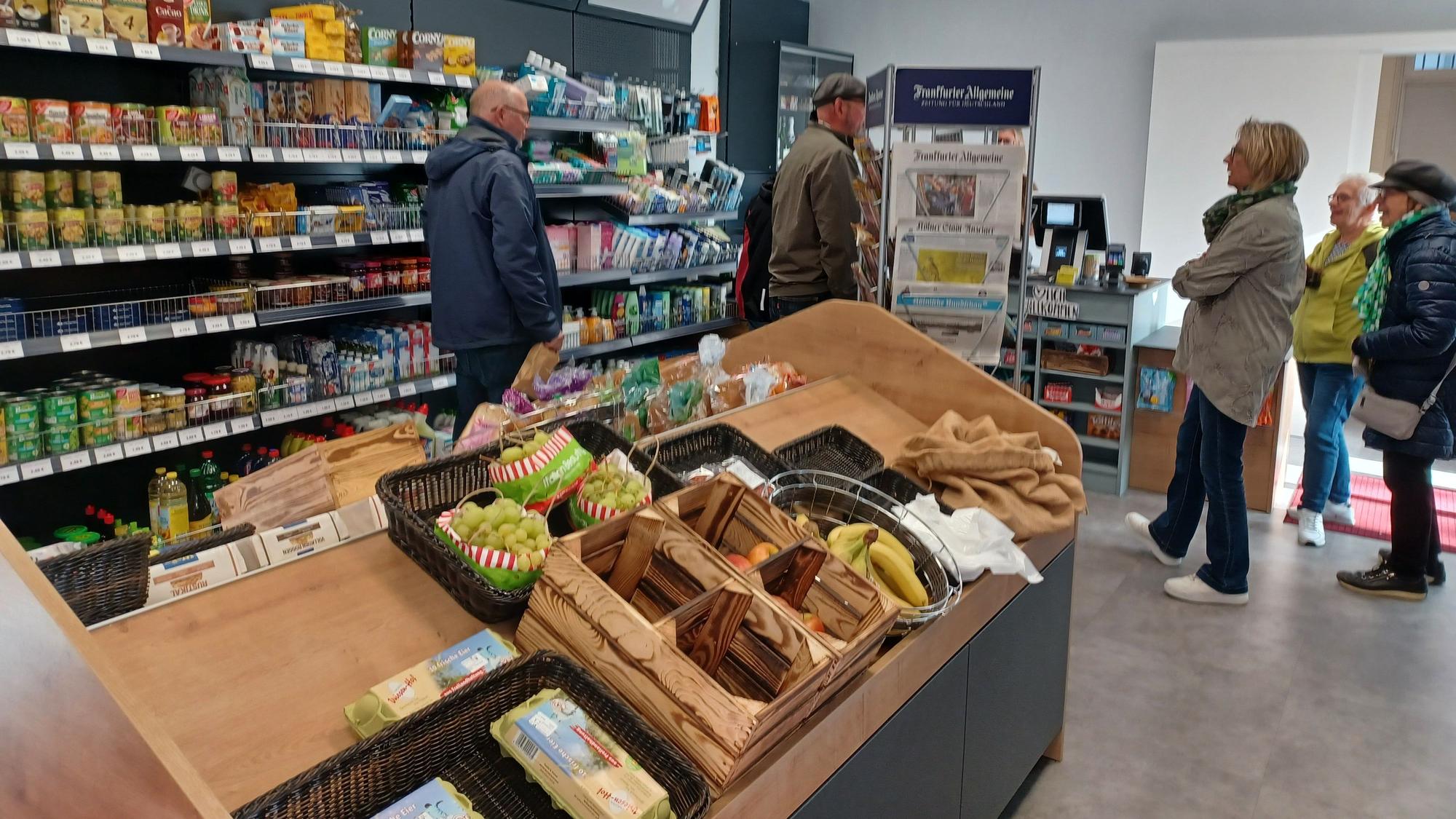 In einem kleinen Laden mit Regalen und Aufstellern stehen Menschen.