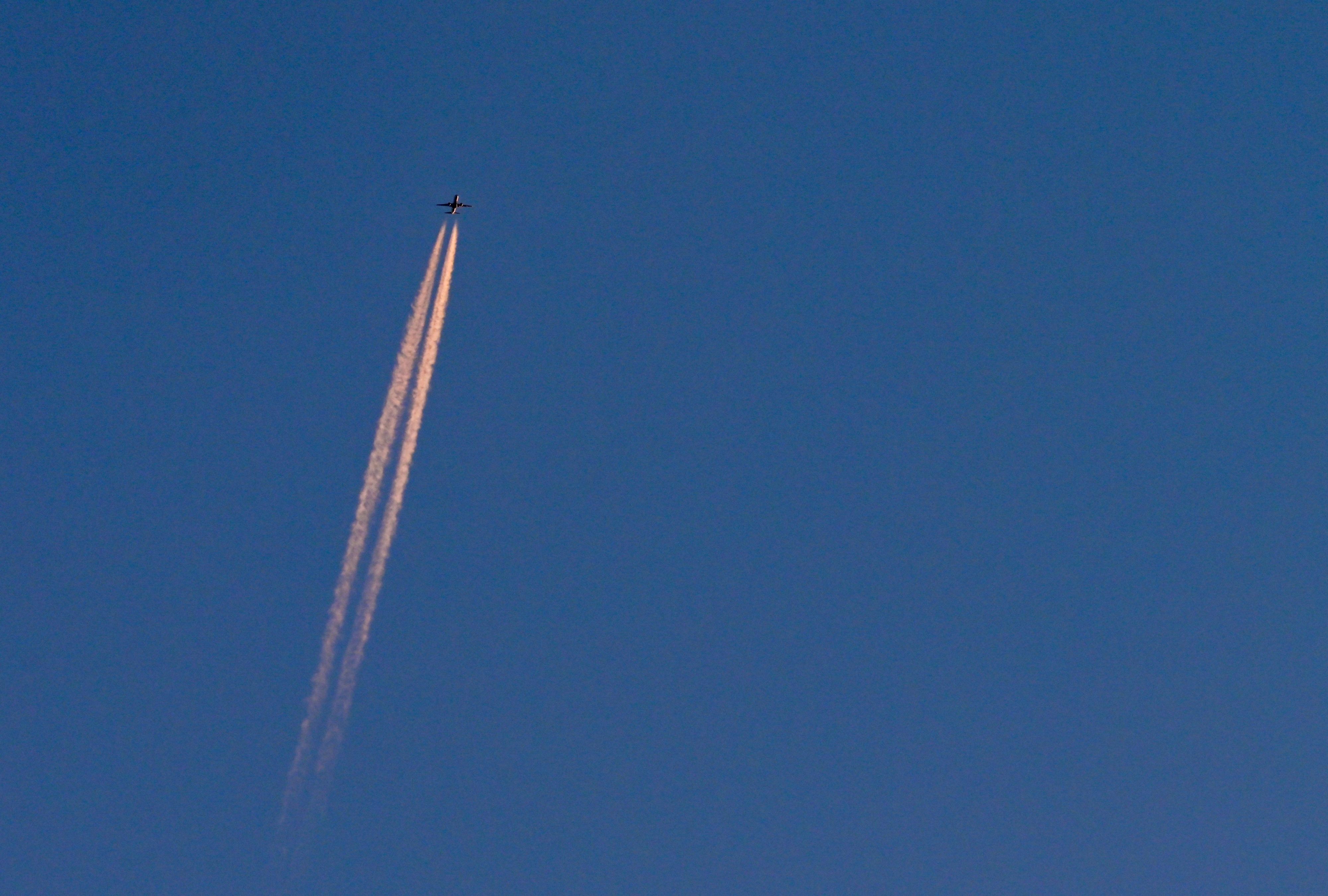 Am blauen Himmel fliegt ein Flugzeug und hinterlässt Kondensstreifen. (Symbolbild)