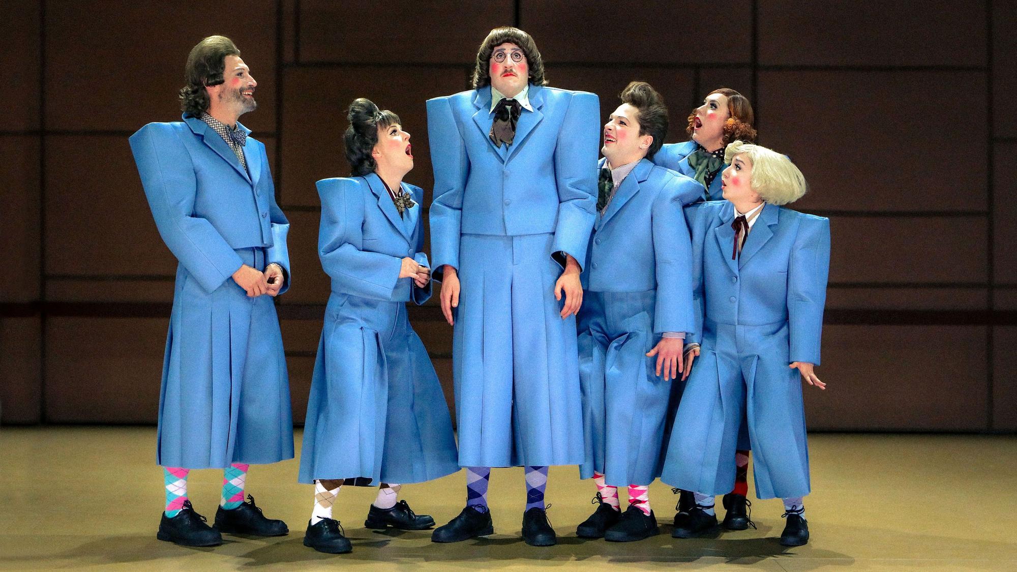 Sechs Schauspieler tragen blaue Anzüge.