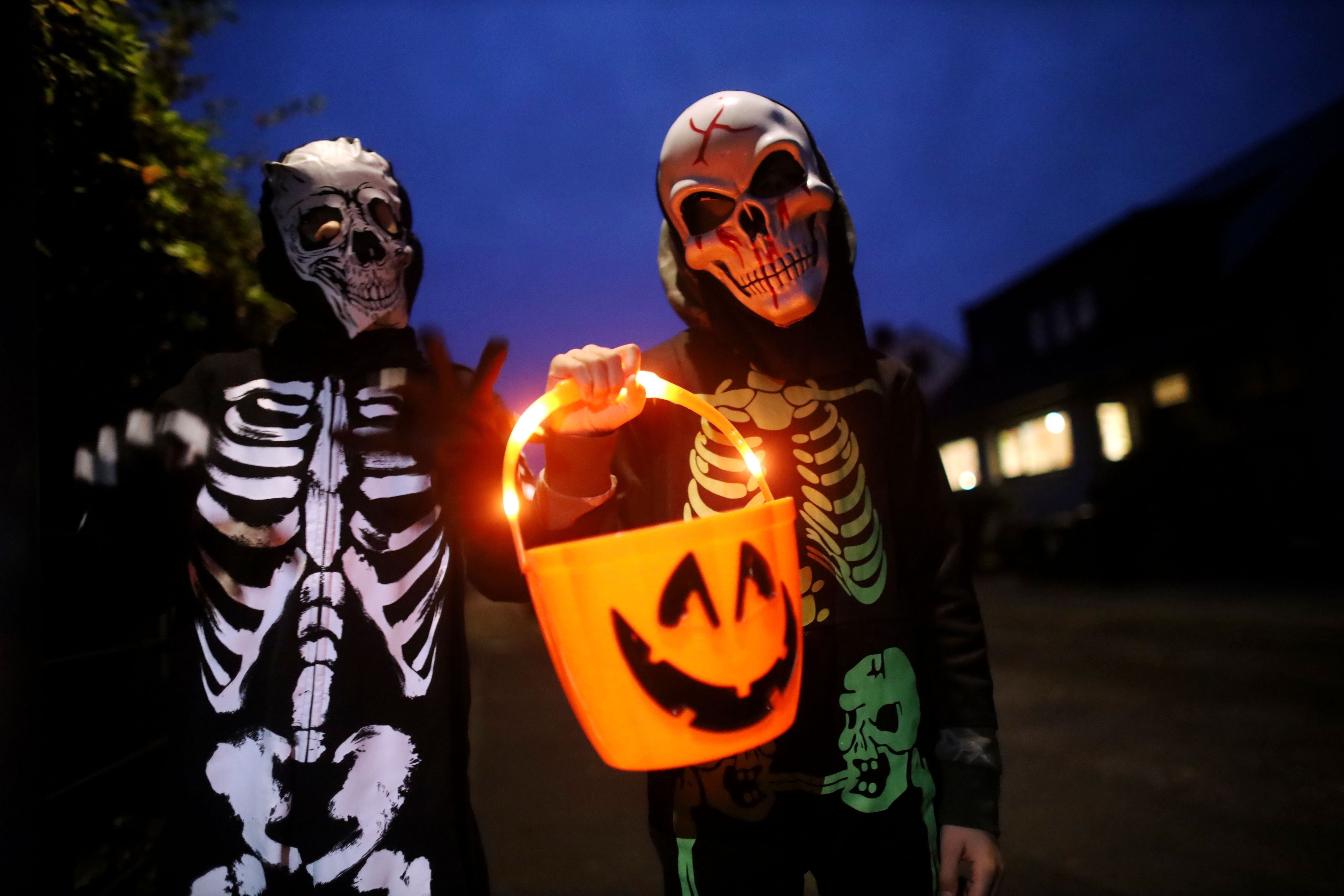 Zwei als Skelett verkleidete Kinder tragen einen leuchtenden Halloween-Eimer.