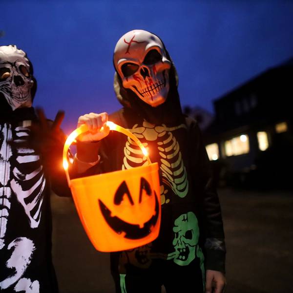 Zwei als Skelett verkleidete Kinder tragen einen leuchtenden Halloween-Eimer.