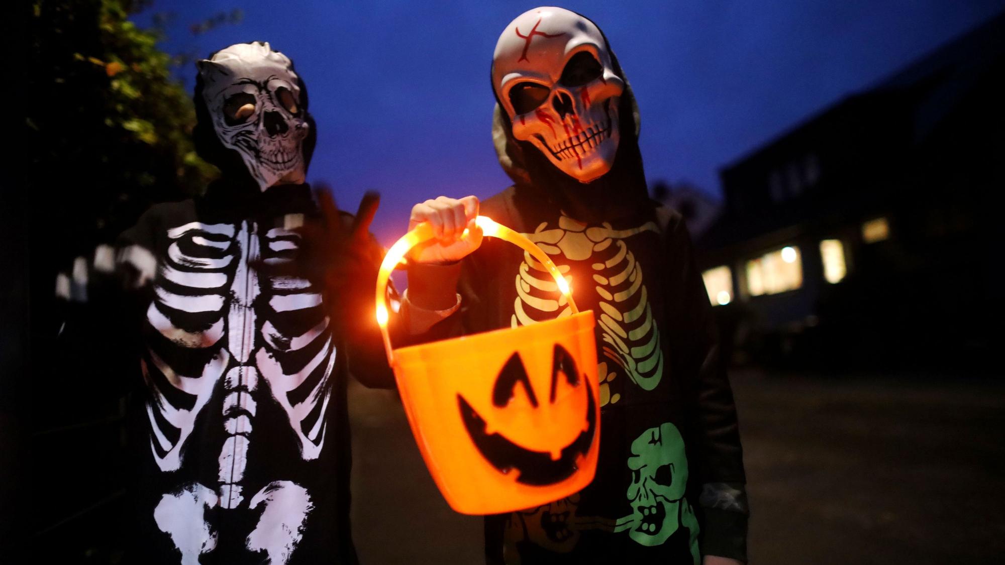 Zwei als Skelett verkleidete Kinder tragen einen leuchtenden Halloween-Eimer.