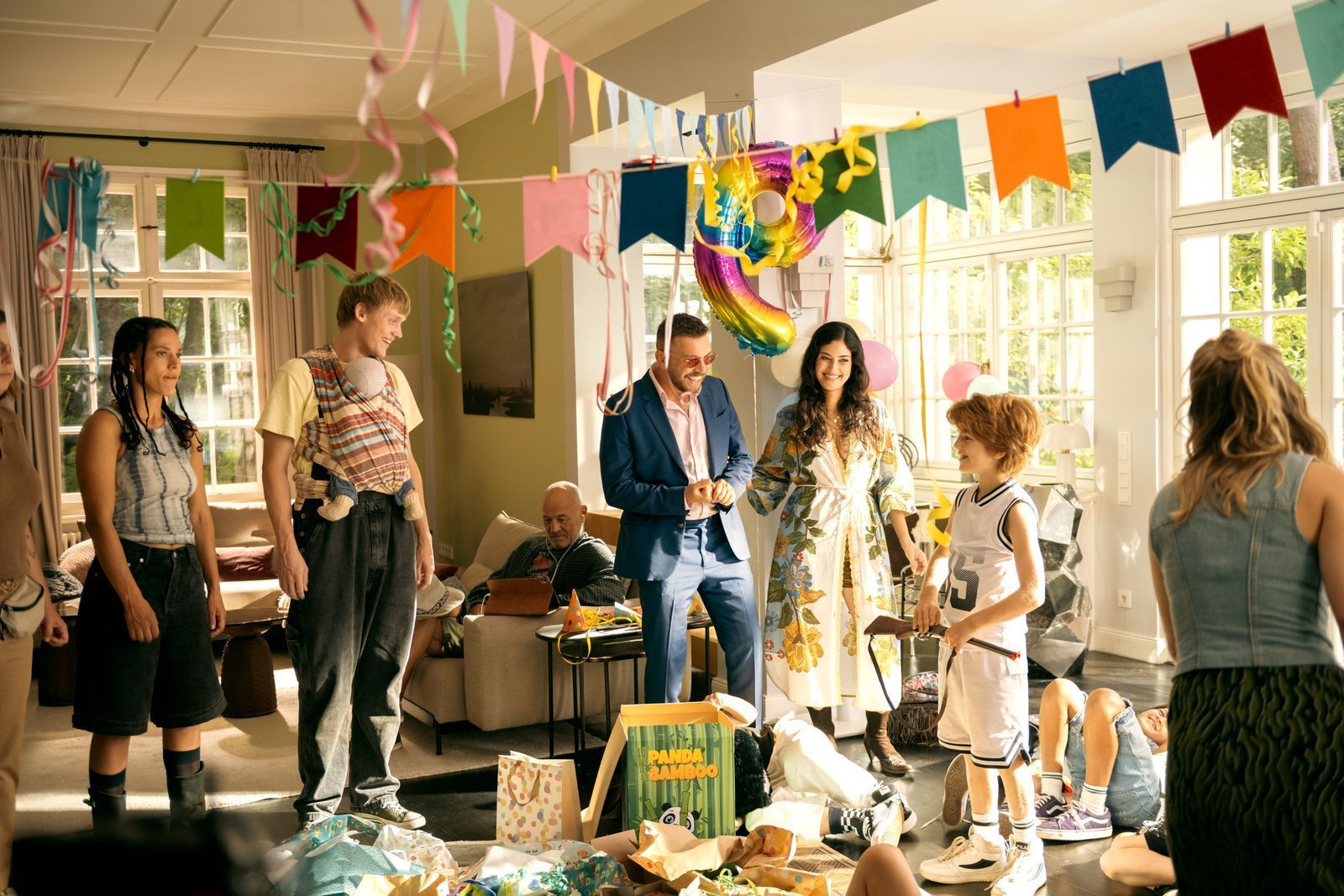 Theo (Levin Wopp, zweiter von rechts) freut sich über das Geschenk von Timo (Edin Hasanović, vierter von links). Seiner Mutter (Jeanne Goursaud, rechts), ihren Freunden Jenny (Amal Keller, links) und Lucas (Enzo Brumm, zweiter von links) sowie Opa Hans (Heiner Lauterbach) und Timos Freundin Sofia (Sogol Faghani) wird das Lachen jedoch bald vergehen. (Bild: Nadja Klier/Netflix)