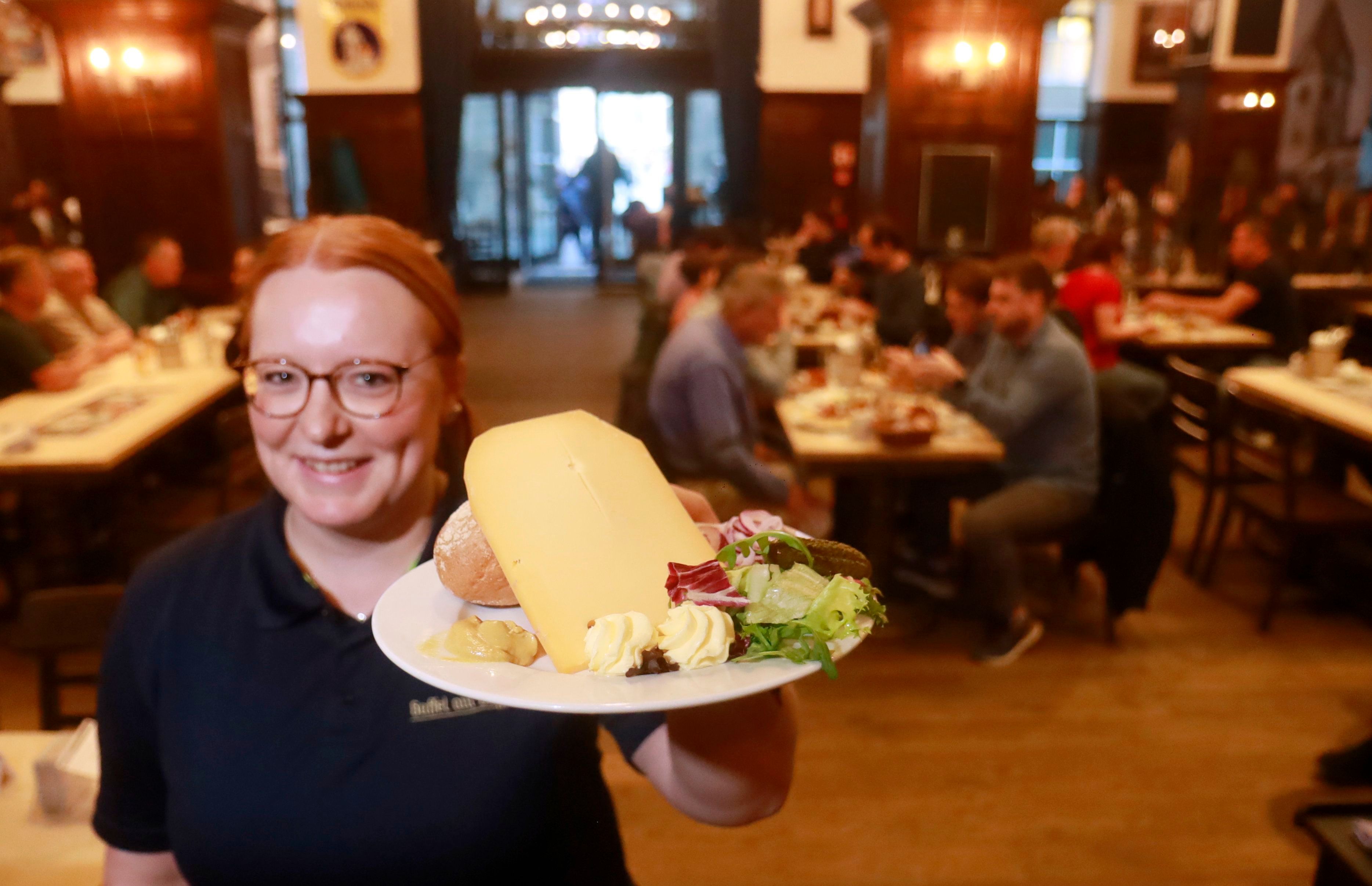 Eine Mitarbeiterin im „Gaffel am Dom“ präsentiert den Brauhaus-Klassiker „Halve Hahn“ mit Röggelchen und einer dicken Scheibe mittelaltem Gouda.