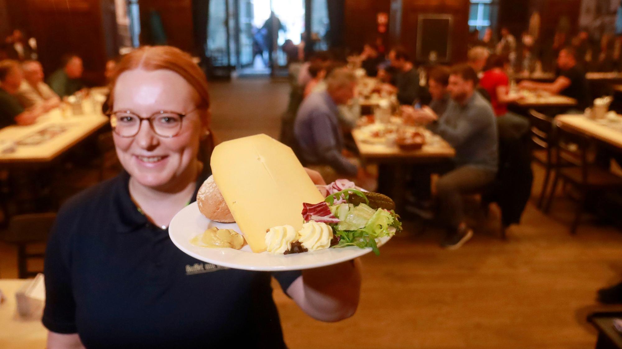 Eine Mitarbeiterin im „Gaffel am Dom“ präsentiert den Brauhaus-Klassiker „Halve Hahn“ mit Röggelchen und einer dicken Scheibe mittelaltem Gouda.