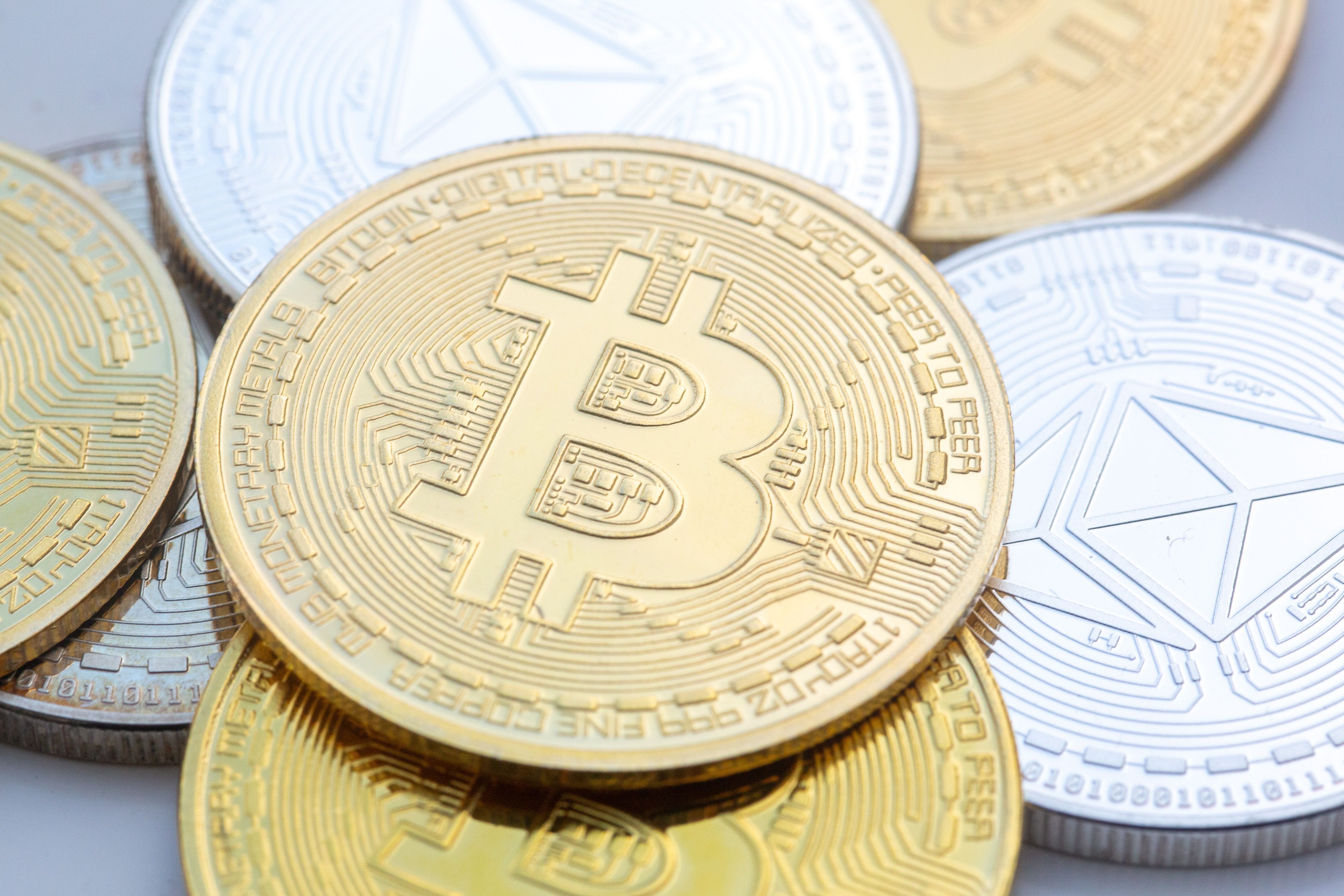 Münzen mit den Symbolen von Bitcoin (M) und Ethereum sind auf einem Tisch angeordnet.