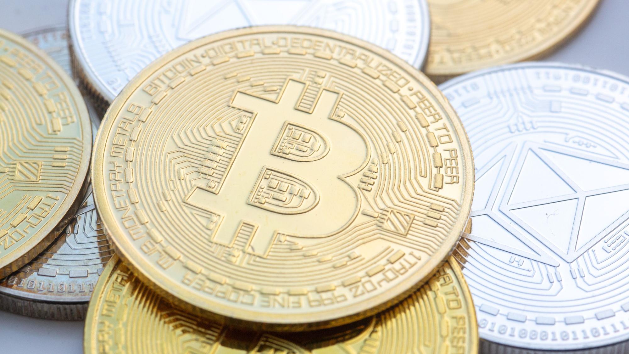 Münzen mit den Symbolen von Bitcoin (M) und Ethereum sind auf einem Tisch angeordnet.