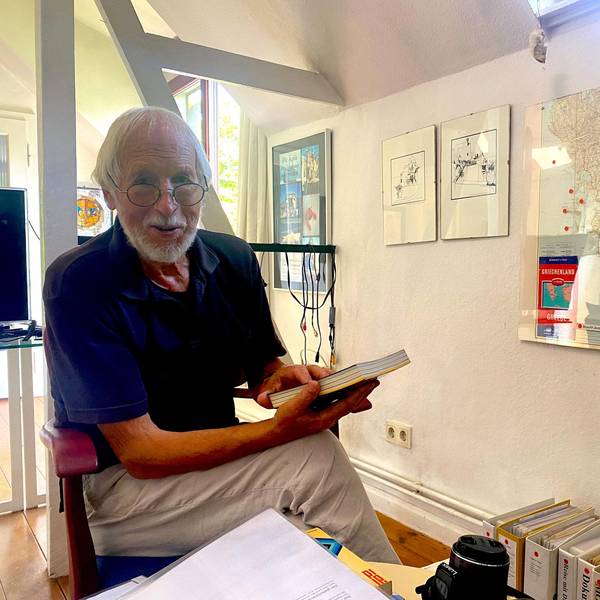 Kurt Schreiner vor einer Weltkarte mit vielen Pins an den bereisten Orten. In der Hand hält er eines von seinen selbstgeschriebenen Reisebüchern.