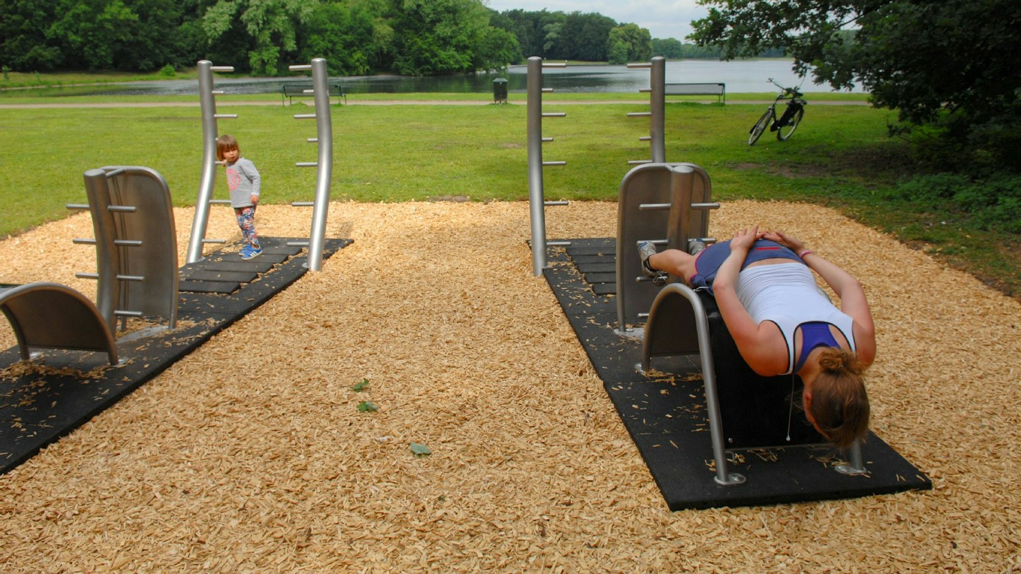 Eine Frau trainiert auf einem Sportgerät in einem Park in Köln.