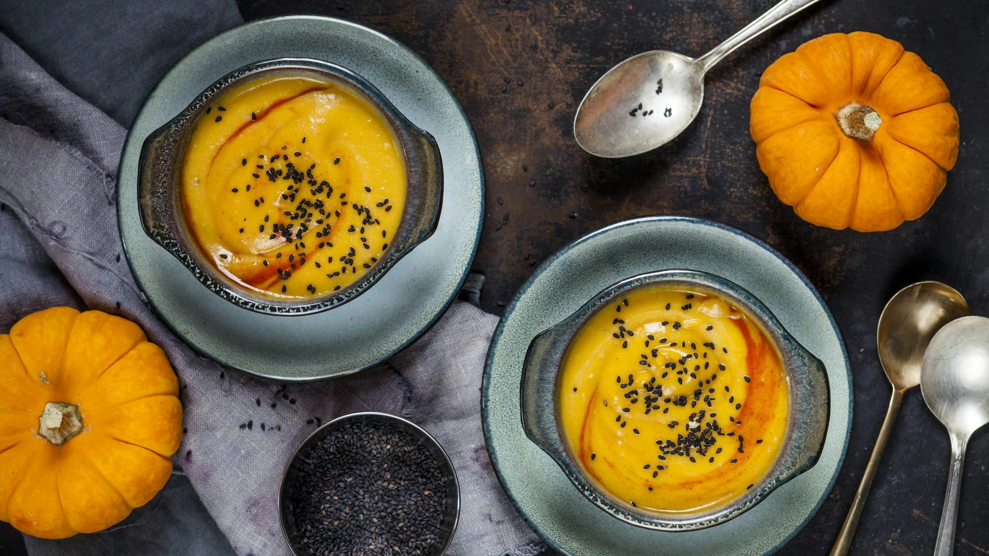 zwei Schalen mit Kürbissuppe, daneben zwei Kürbisse