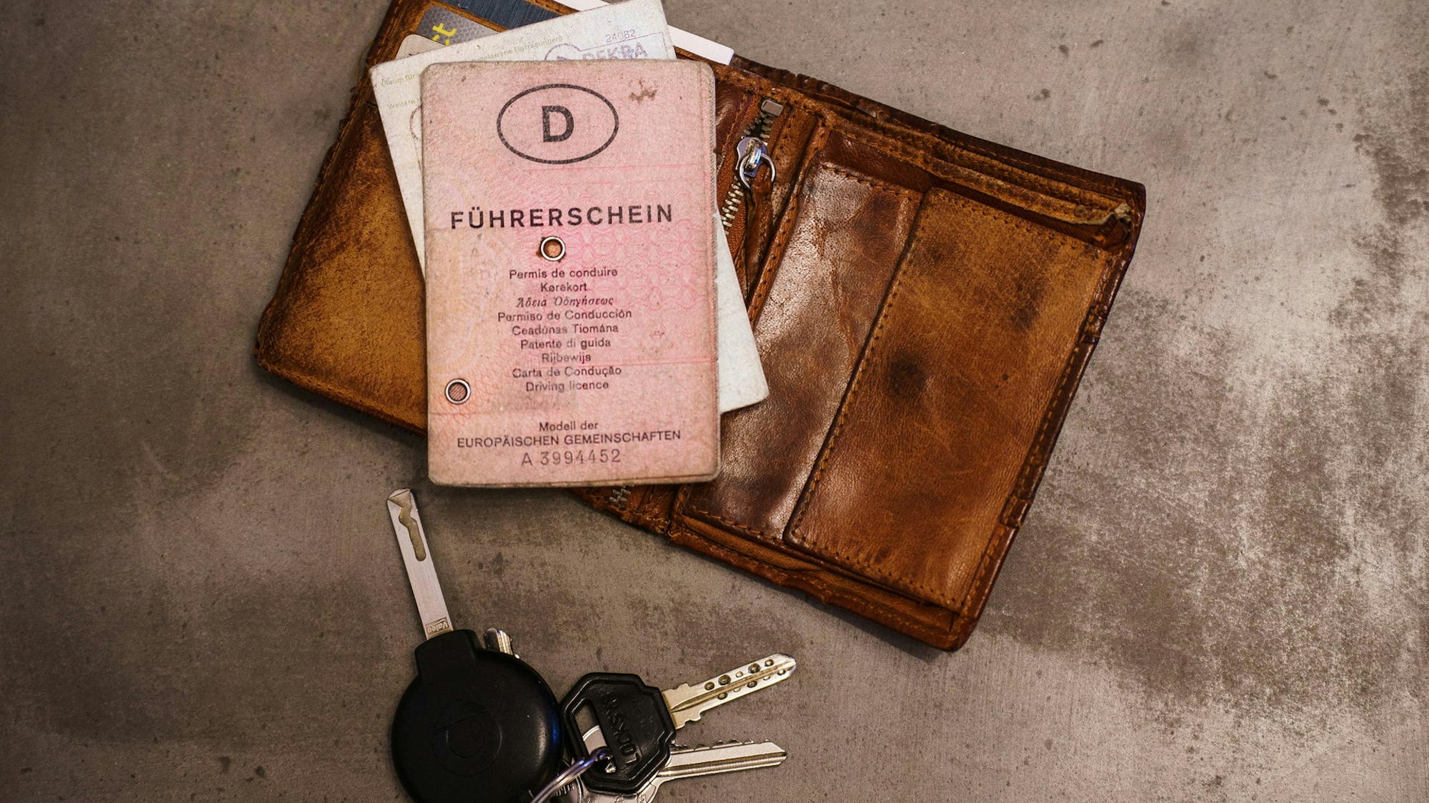 Das Foto zeigt einen rosa Führerschein, ein Portemonnaie und einen Schlüsselbund