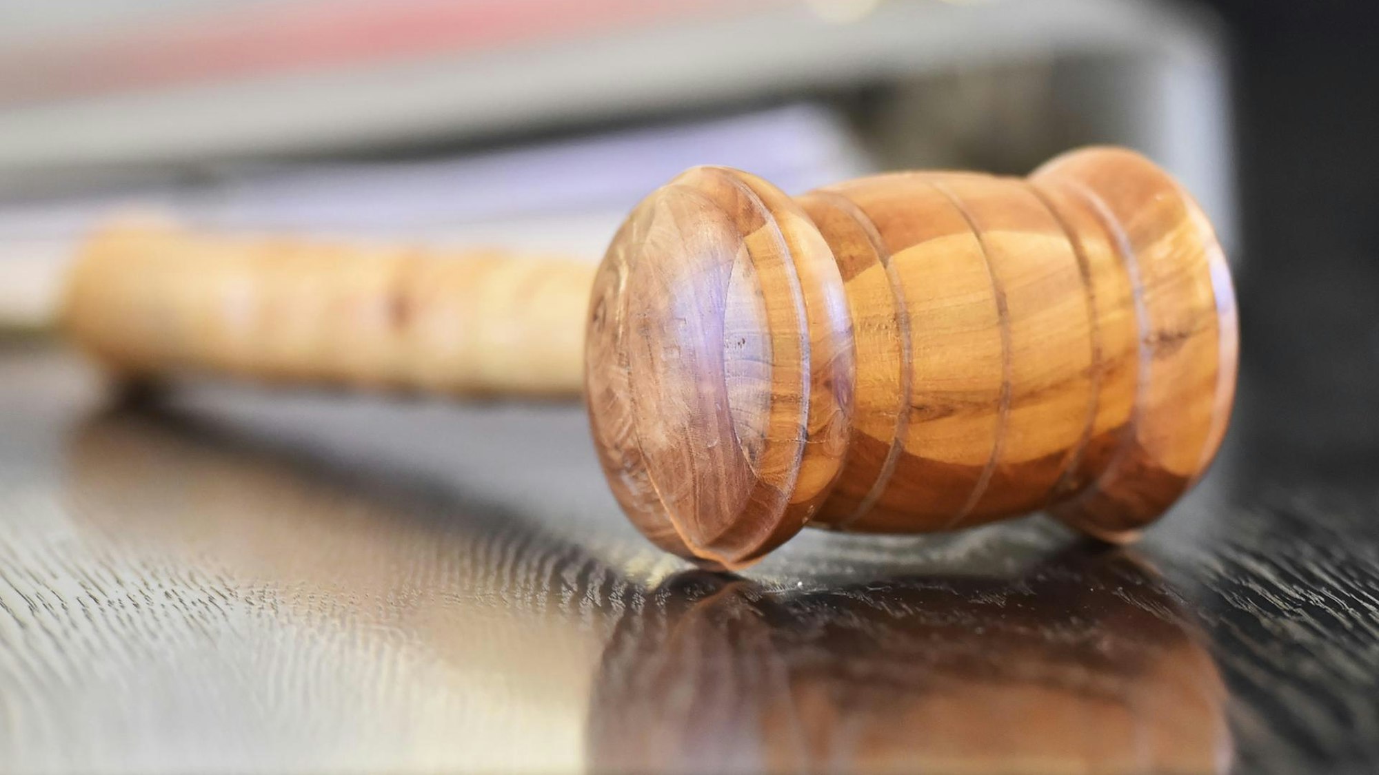 Das Symbolbild zeigt einen Holzhammer, der auf einer schwarzen Tischplatte liegt.