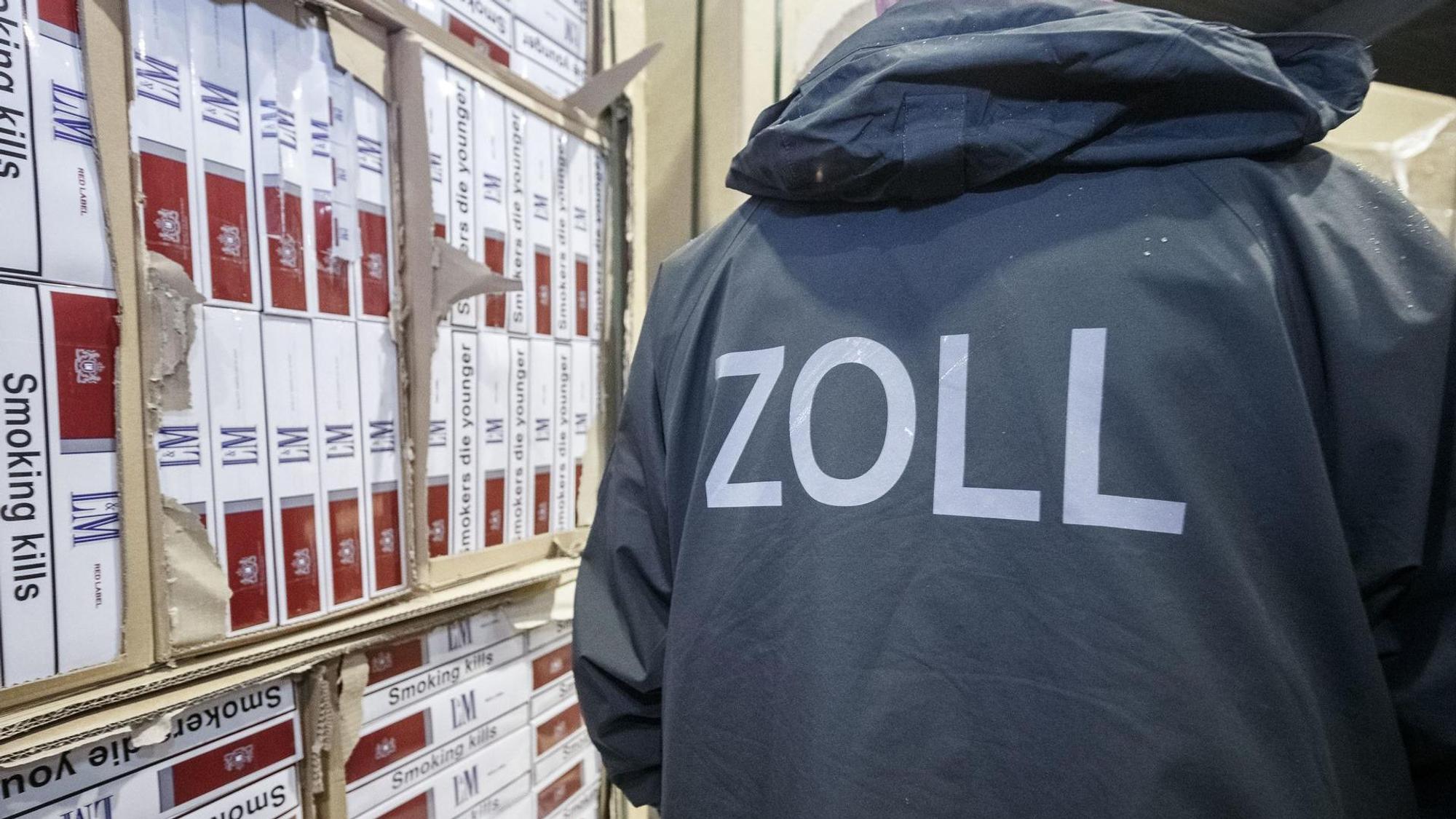 Ein Zollbeamter steht neben einem Regal mit sichergestellten Zigaretten.