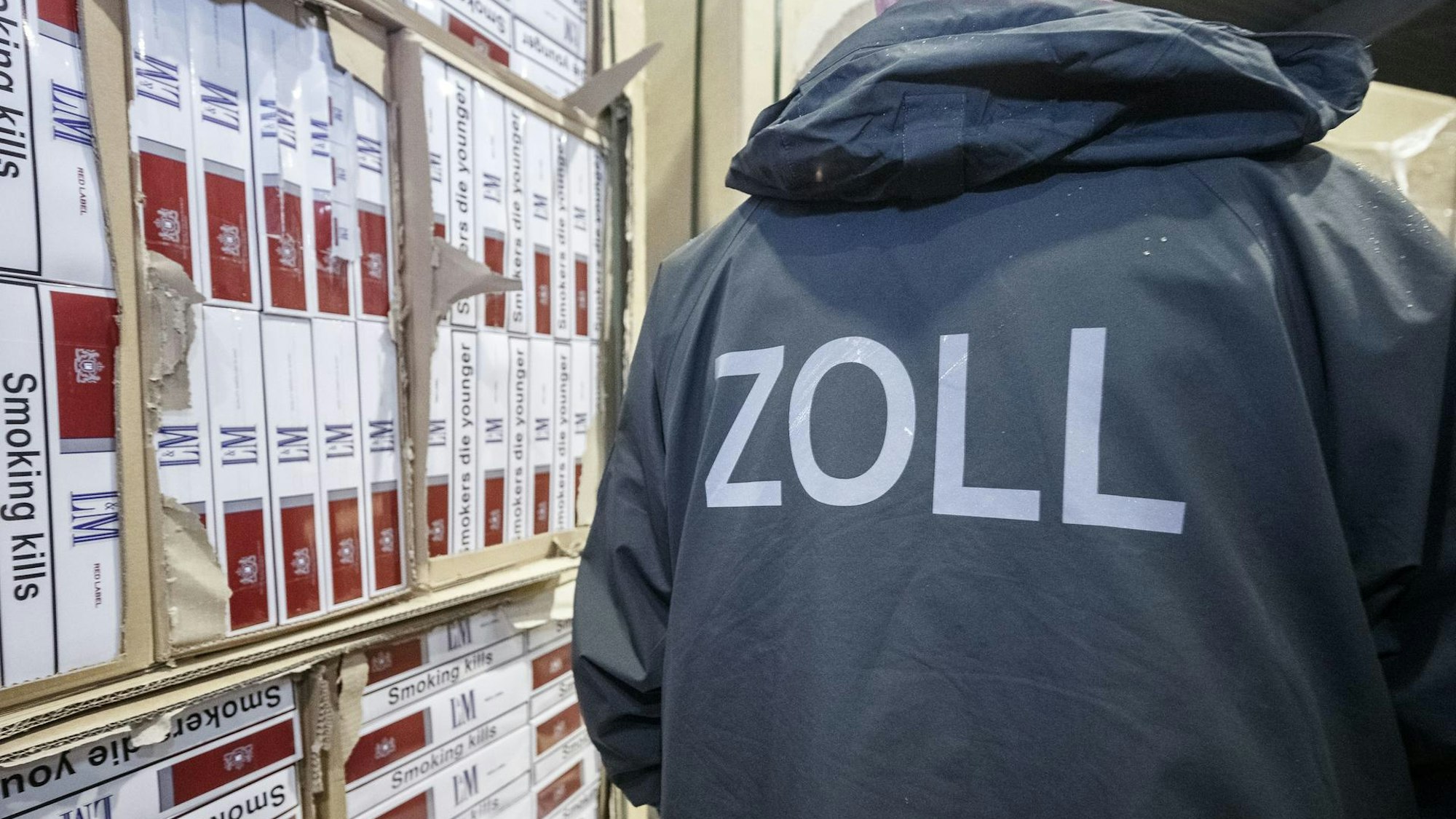 Ein Zollbeamter steht neben einem Regal mit sichergestellten Zigaretten.