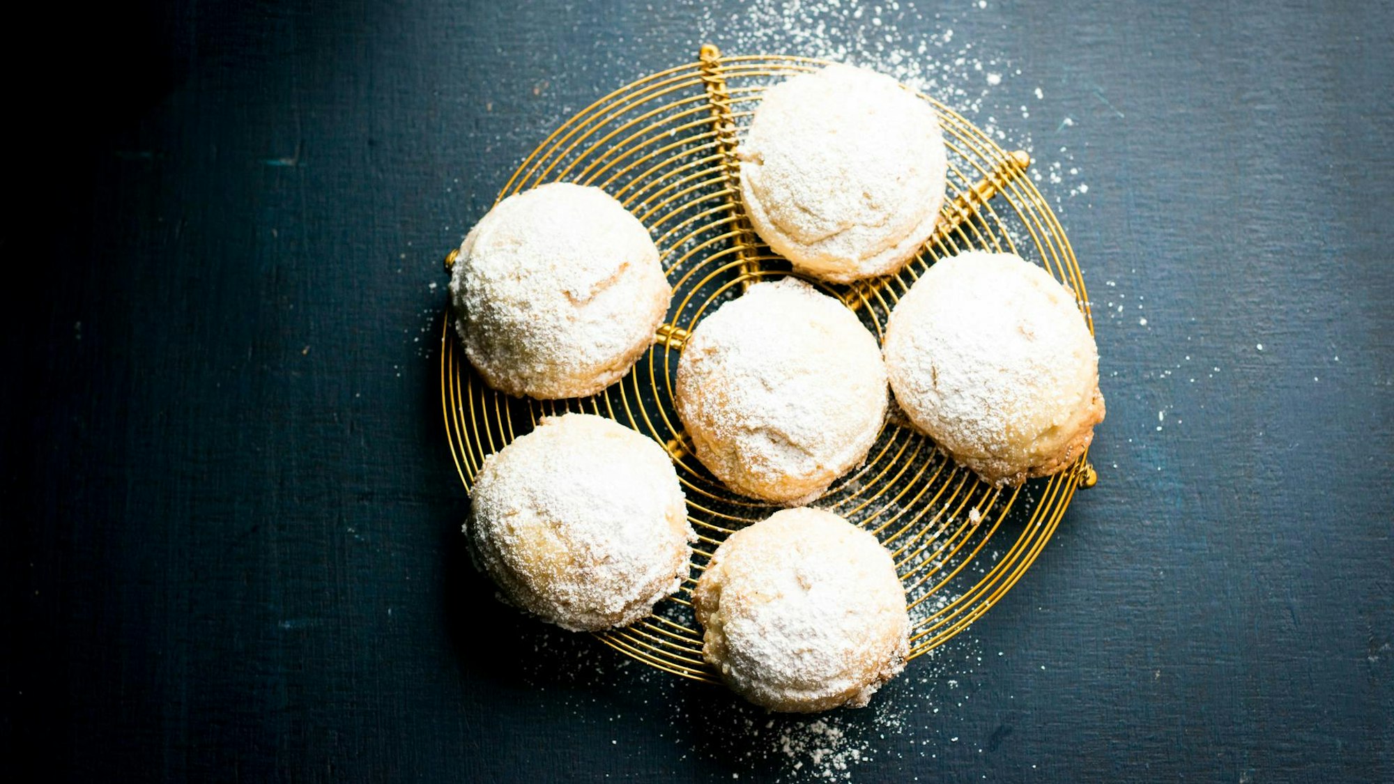 Mit Puderzucker bestäubte Macadamia-Keks-Kissen liegen auf einem Teller angerichtet.