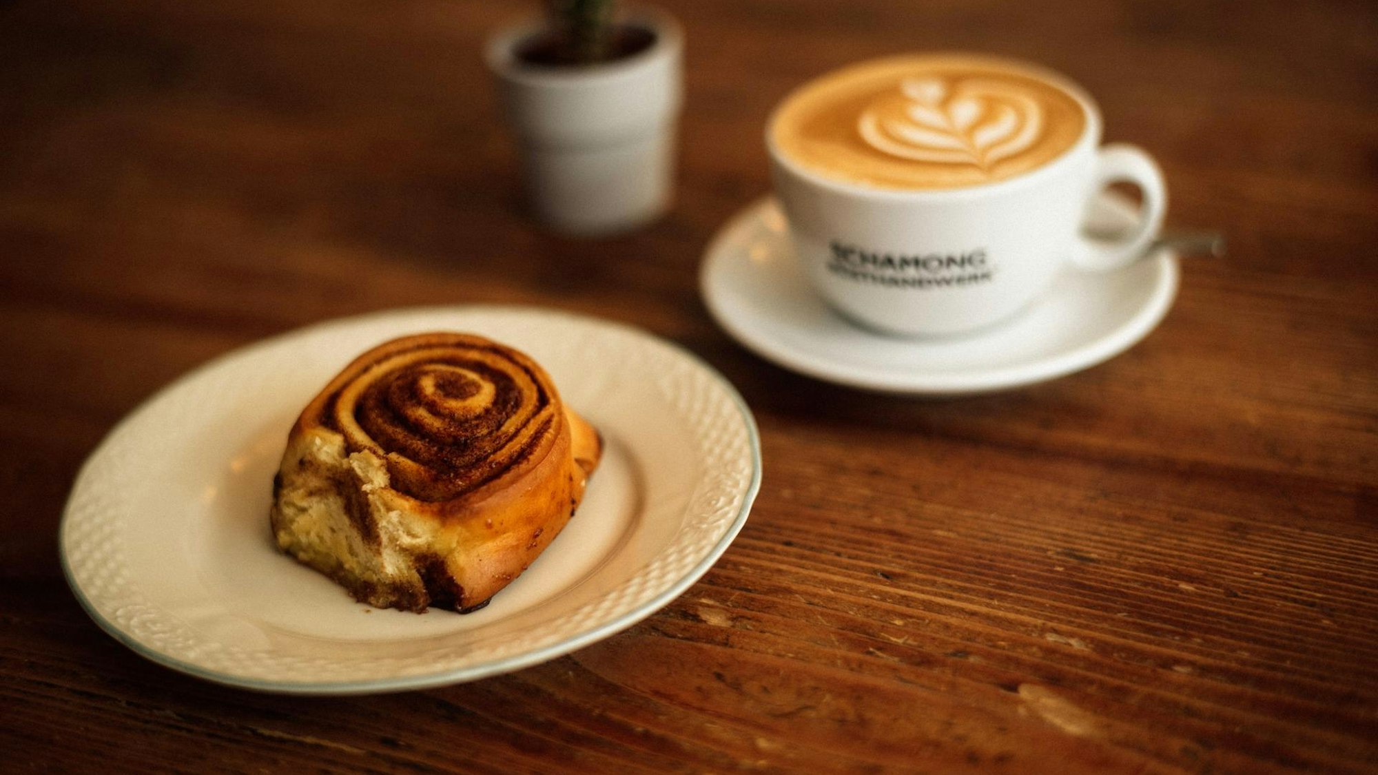 Eine Zimtschnecke liegt auf einem Teller, daneben steht ein Kaffee