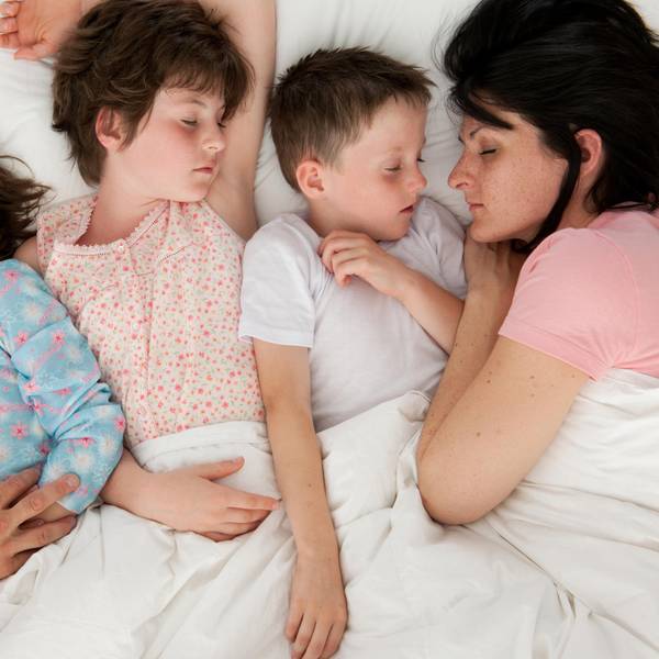 Eltern schlafen mit drei Kindern in einem Bett.